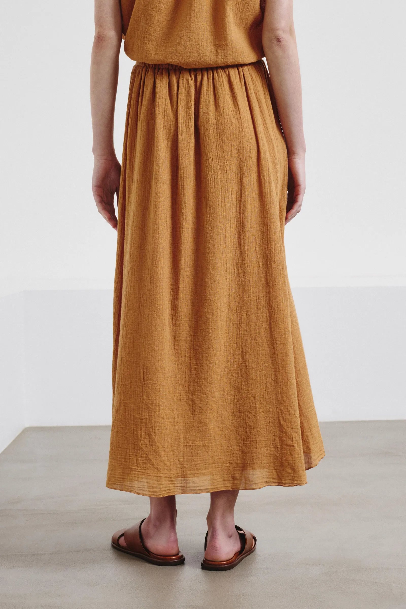 Person wearing a mustard yellow skirt and top on a plain background