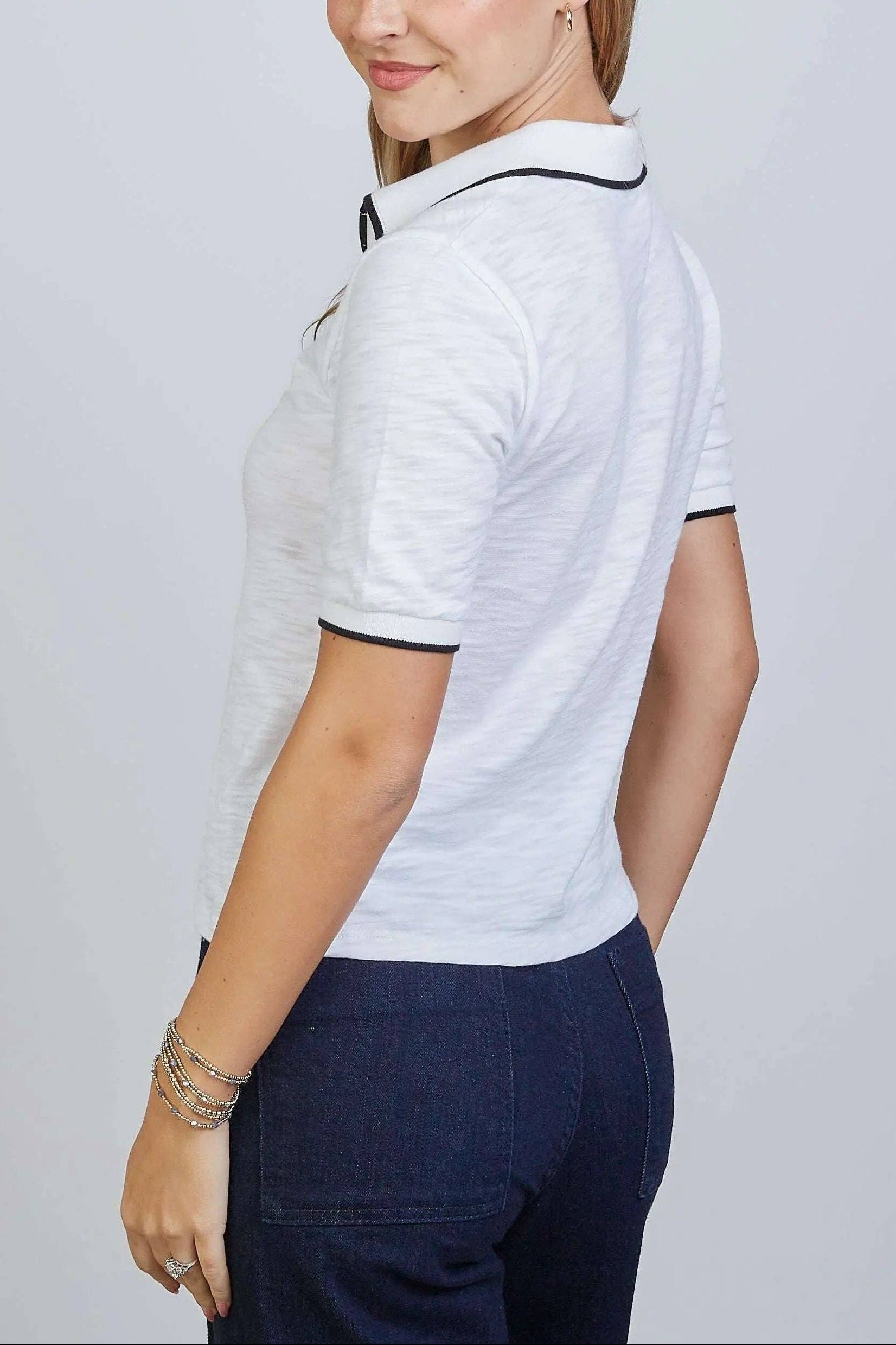 Woman wearing a white polo shirt with black trim on a plain background