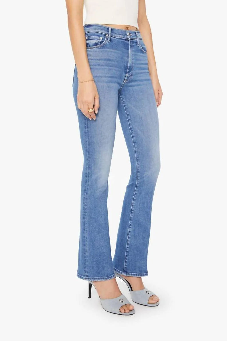 A model wearing light-wash blue flare jeans, a white ribbed tank top, and light blue heeled sandals, shown against a plain light gray studio background.