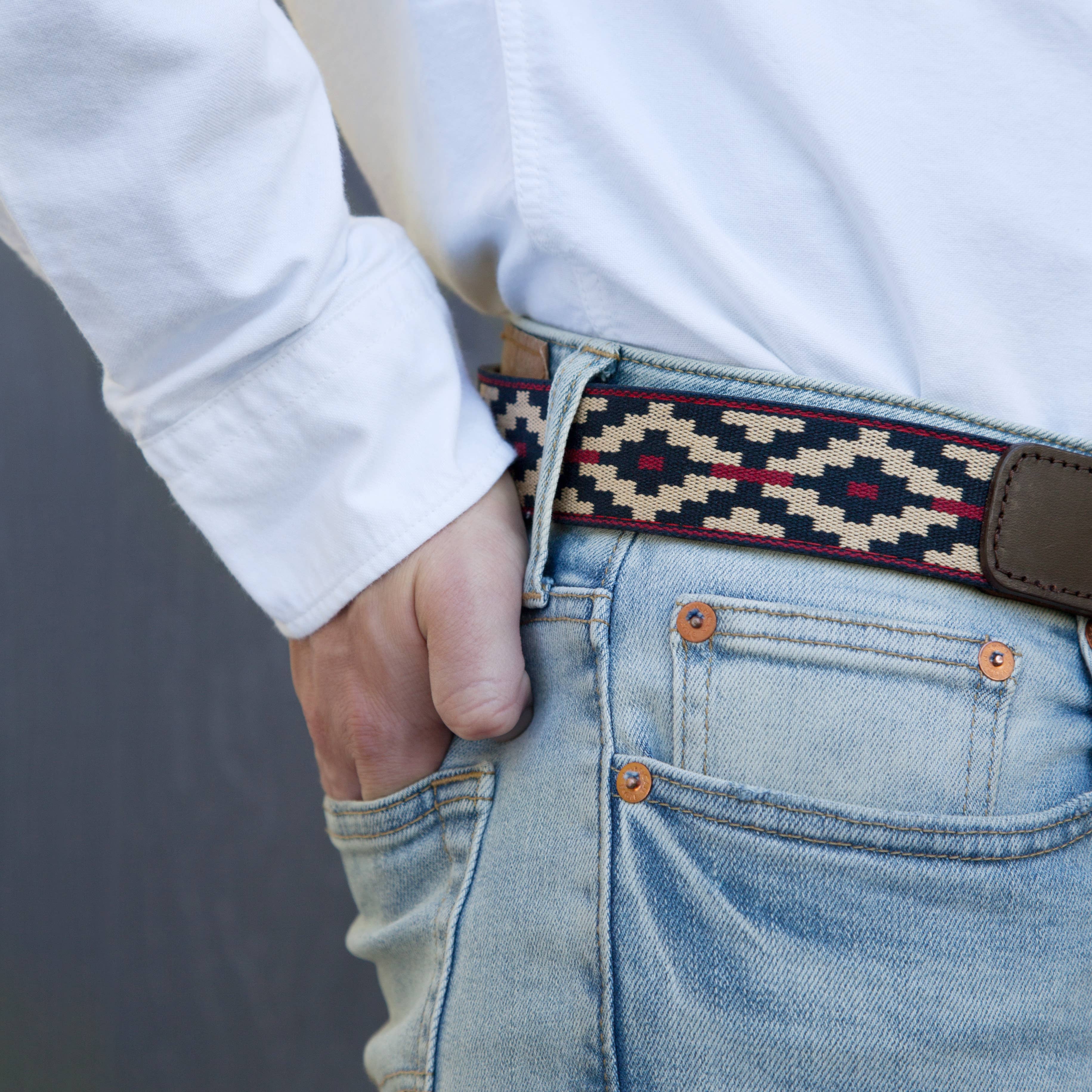 Person wearing a patterned belt with jeans against a neutral background