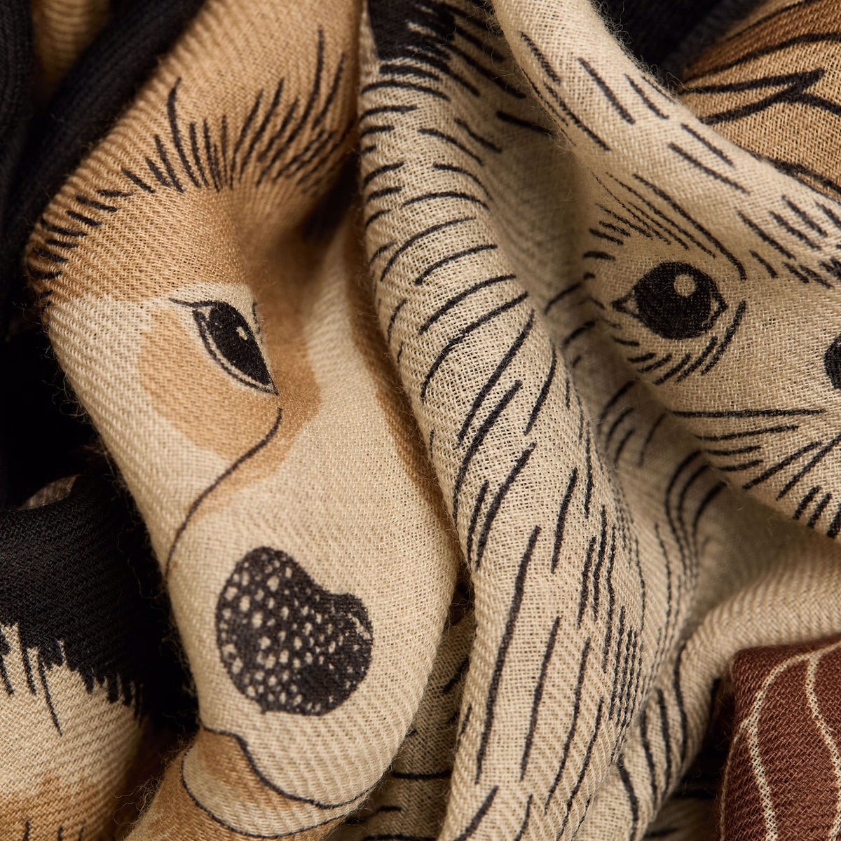 Close-up of a woven scarf featuring illustrated dog faces in beige, tan, black, and brown tones.
