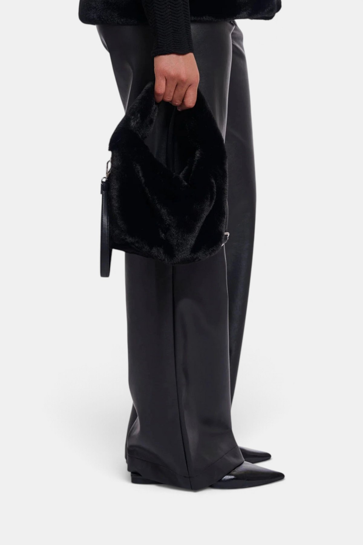 The Copper Shed black faux fur crossbody bag with a zipper closure and removable strap held by a model.