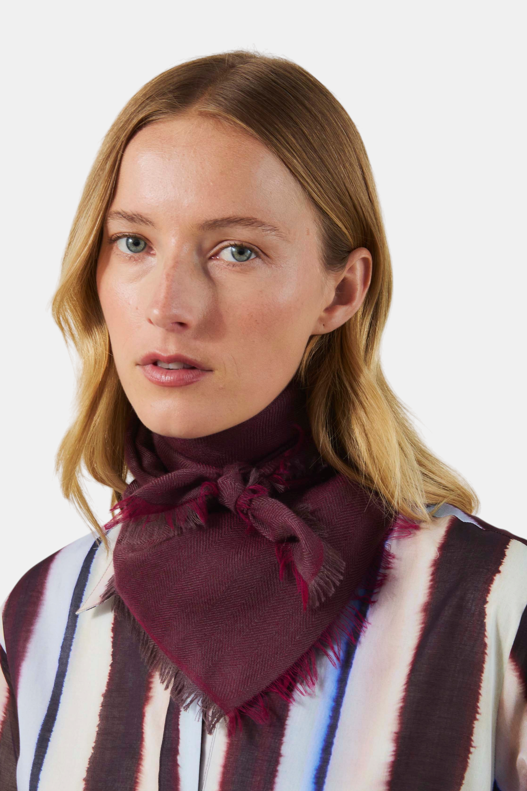 The Copper Shed burgundy cashmere scarf with a herringbone pattern and frayed edges tied around a woman's neck.