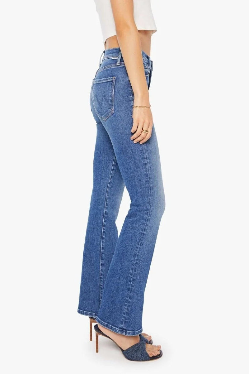A side profile view of a model wearing blue high-waisted flare jeans, styled with a white cropped top and dark blue heeled sandals against a light gray background.
