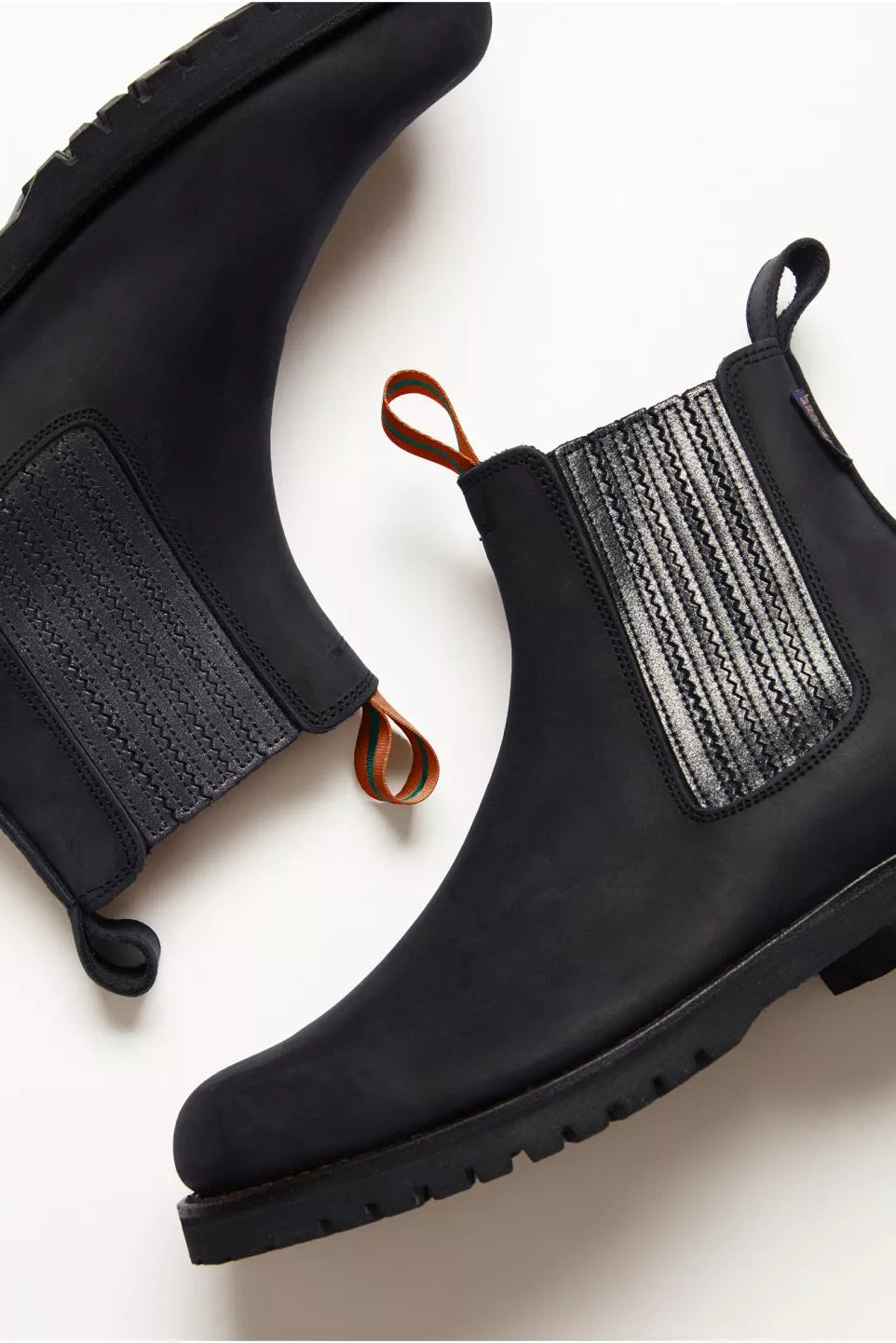 Black Chelsea boots with textured side panels on a light background