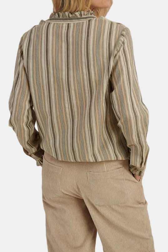 Person wearing a striped shirt and beige pants against a mountainous landscape.