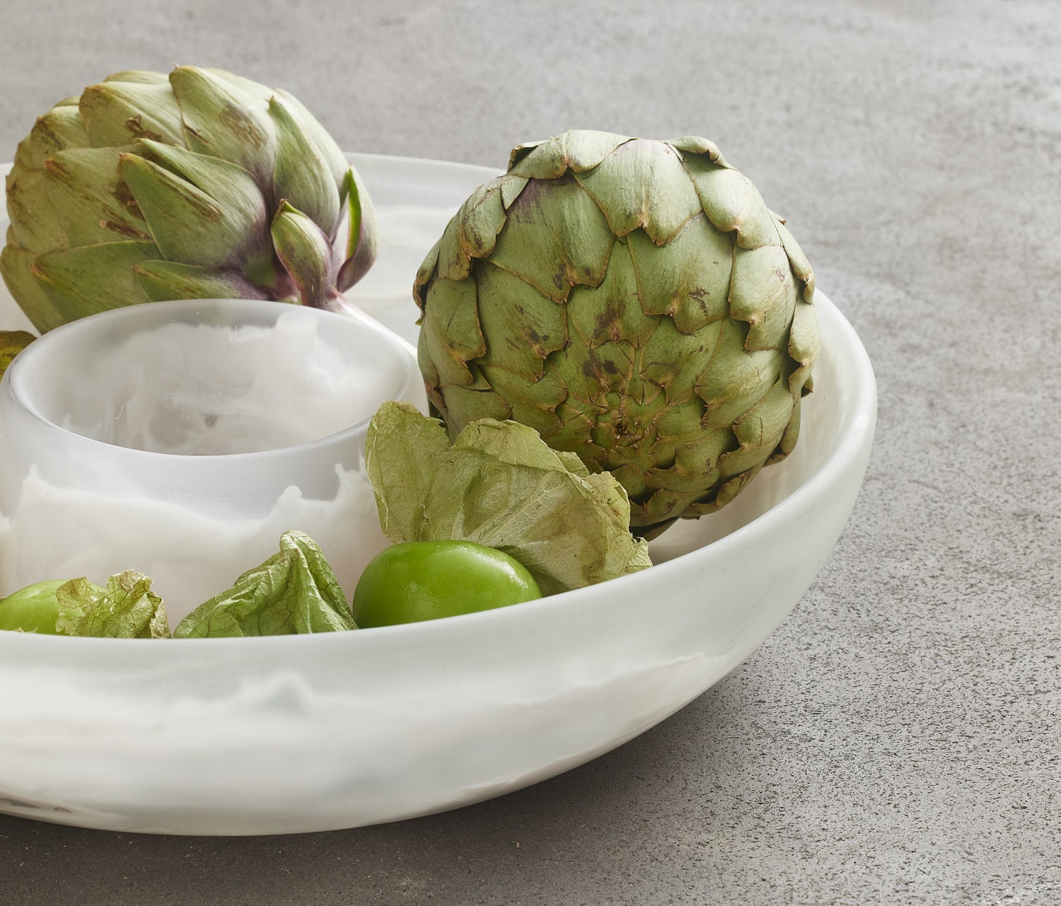 Artichokes in a white bowl on a gray surface