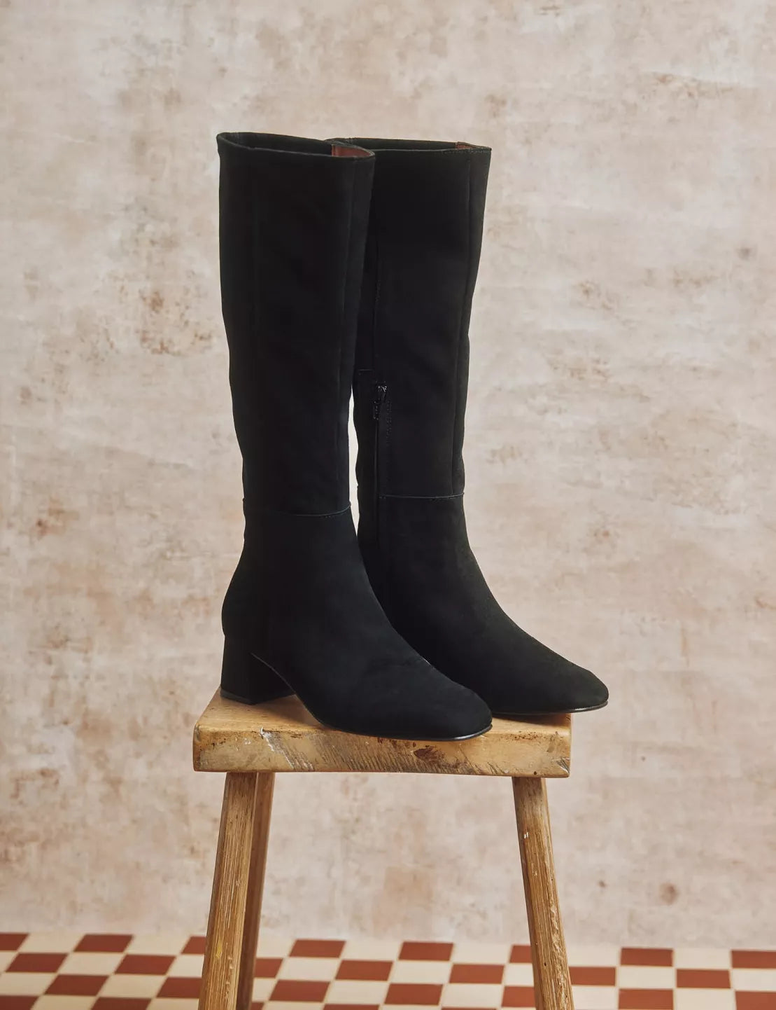 Black knee-high boots on a wooden stool against a textured wall.