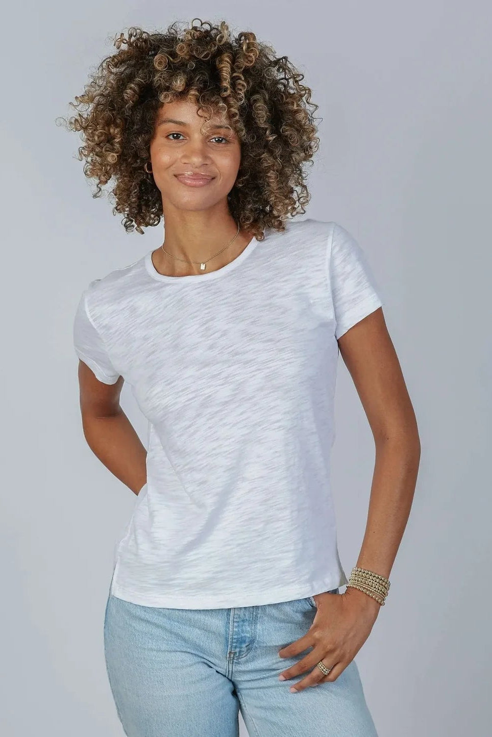Woman wearing a white t-shirt and light blue jeans against a plain background