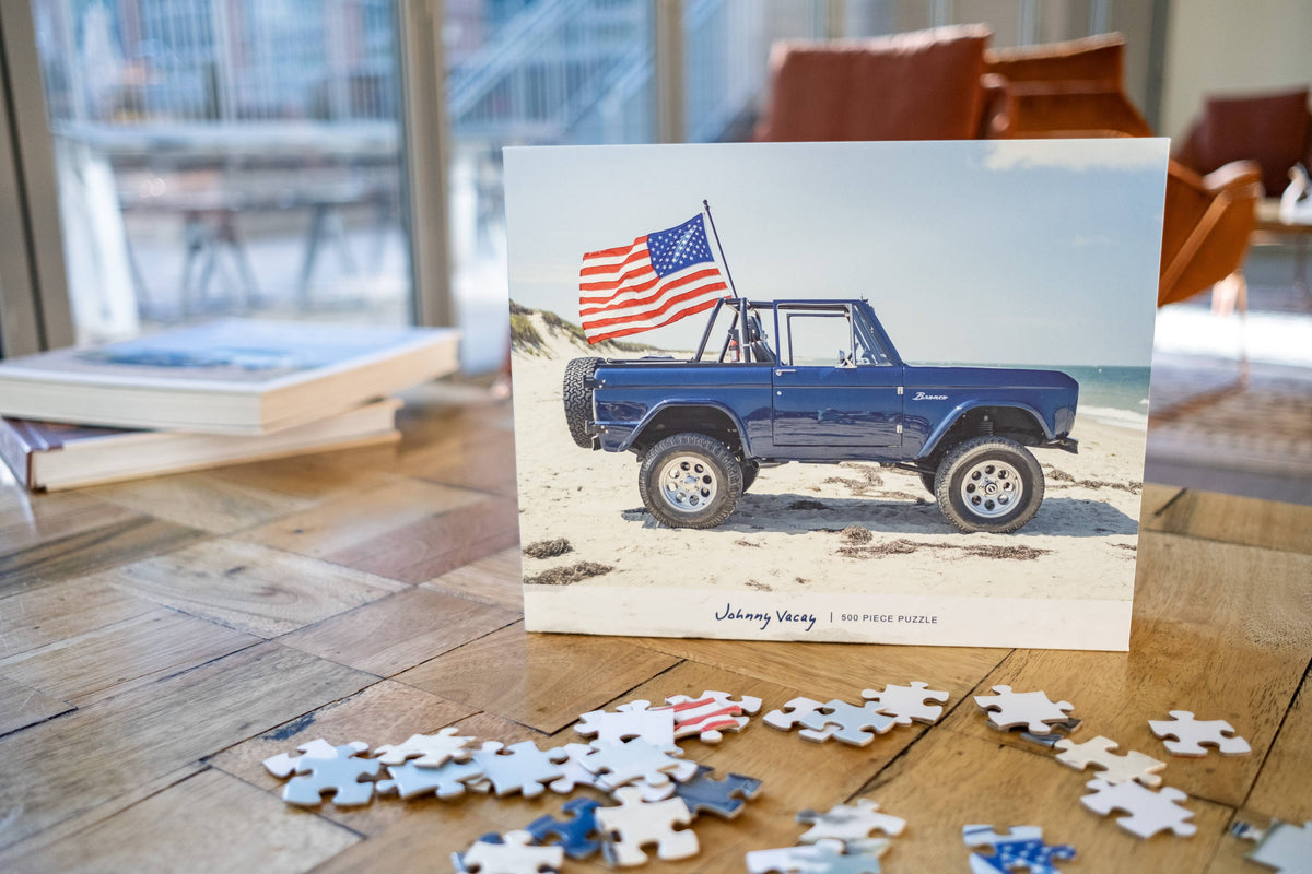 The Copper Shed American Bronco 500 piece puzzle box featuring a blue vintage SUV with an American flag on a beach.