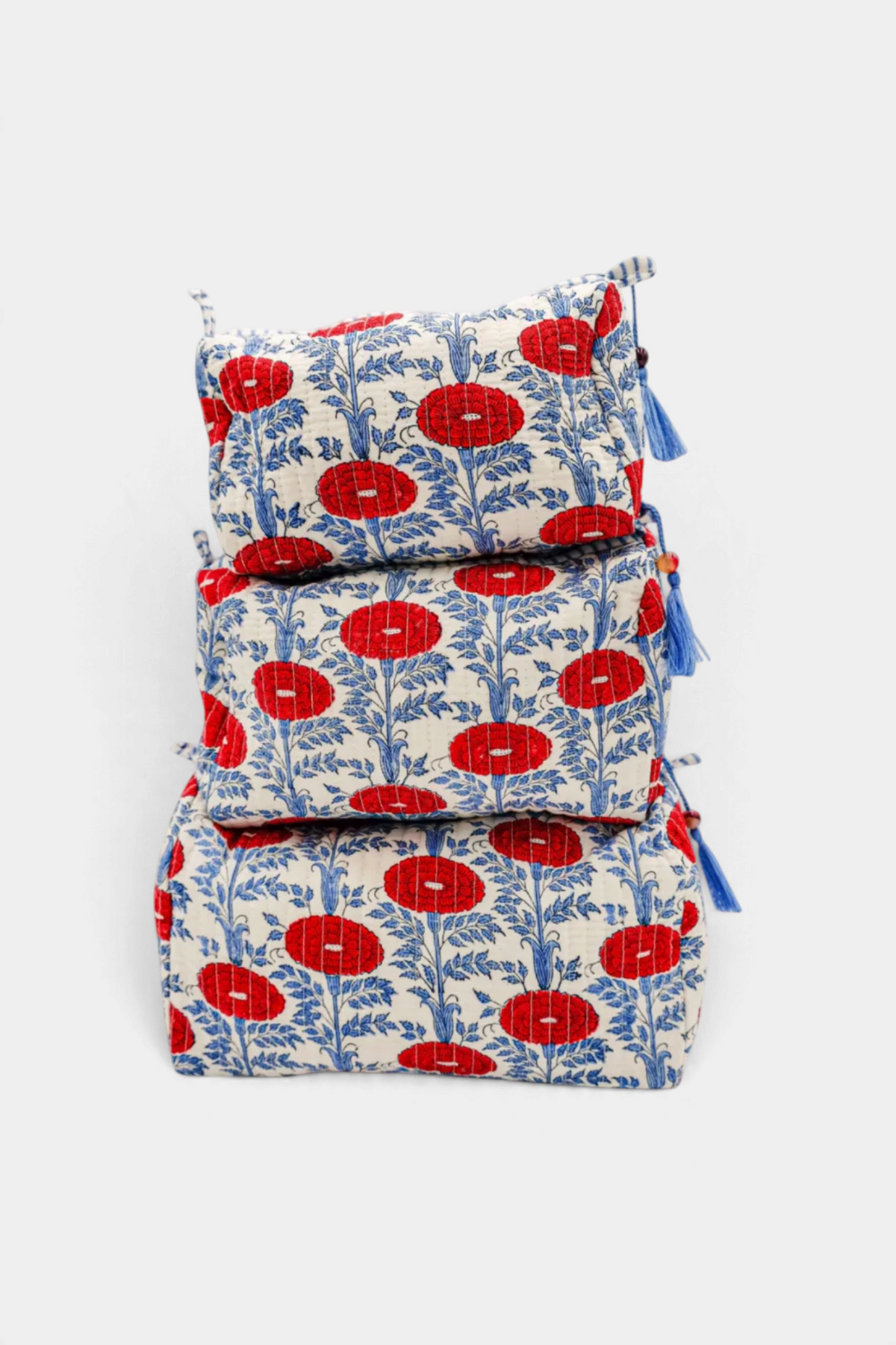 The Copper Shed Araminta medium toiletry bag featuring a red and blue floral block-print pattern with blue tassels.