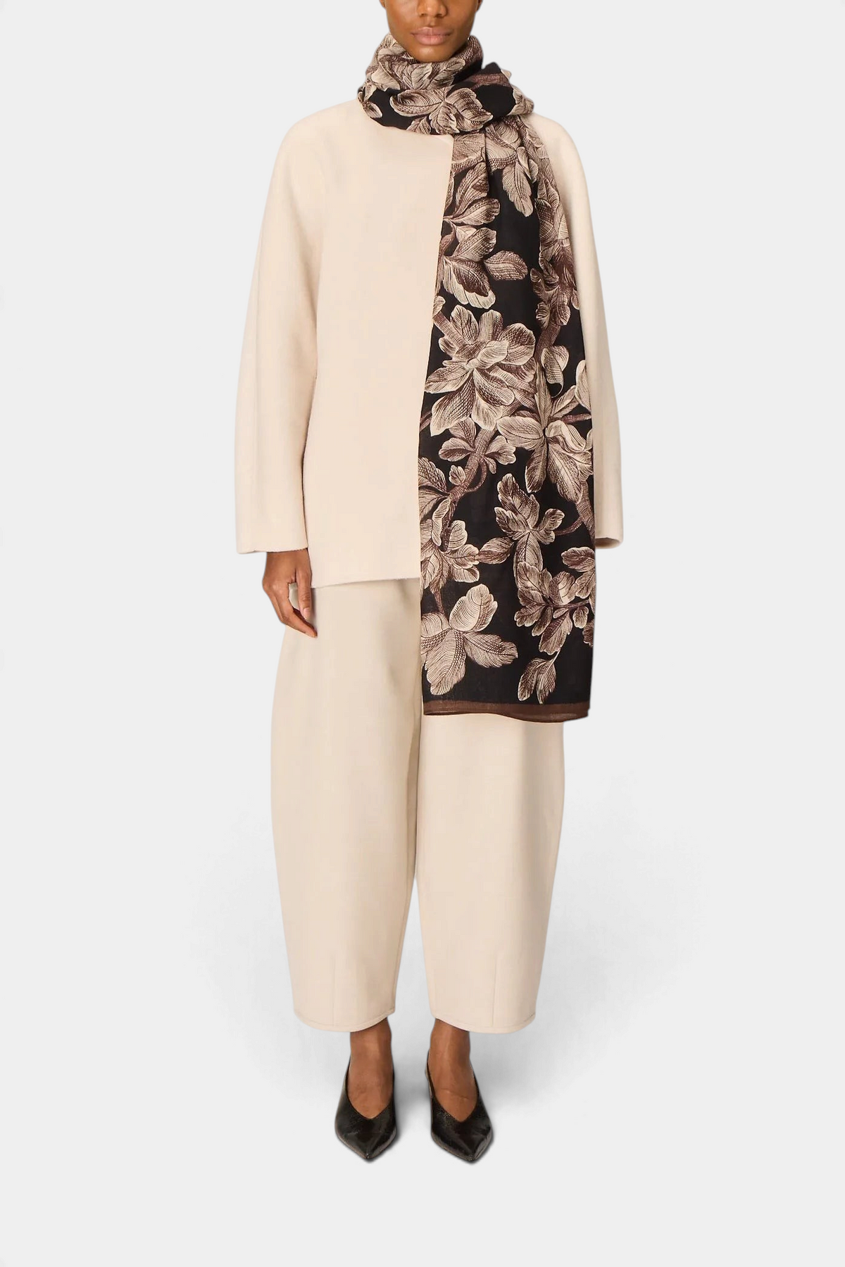 The Copper Shed Arboris black wool scarf with a floral pattern draped over a model wearing a cream-colored outfit.