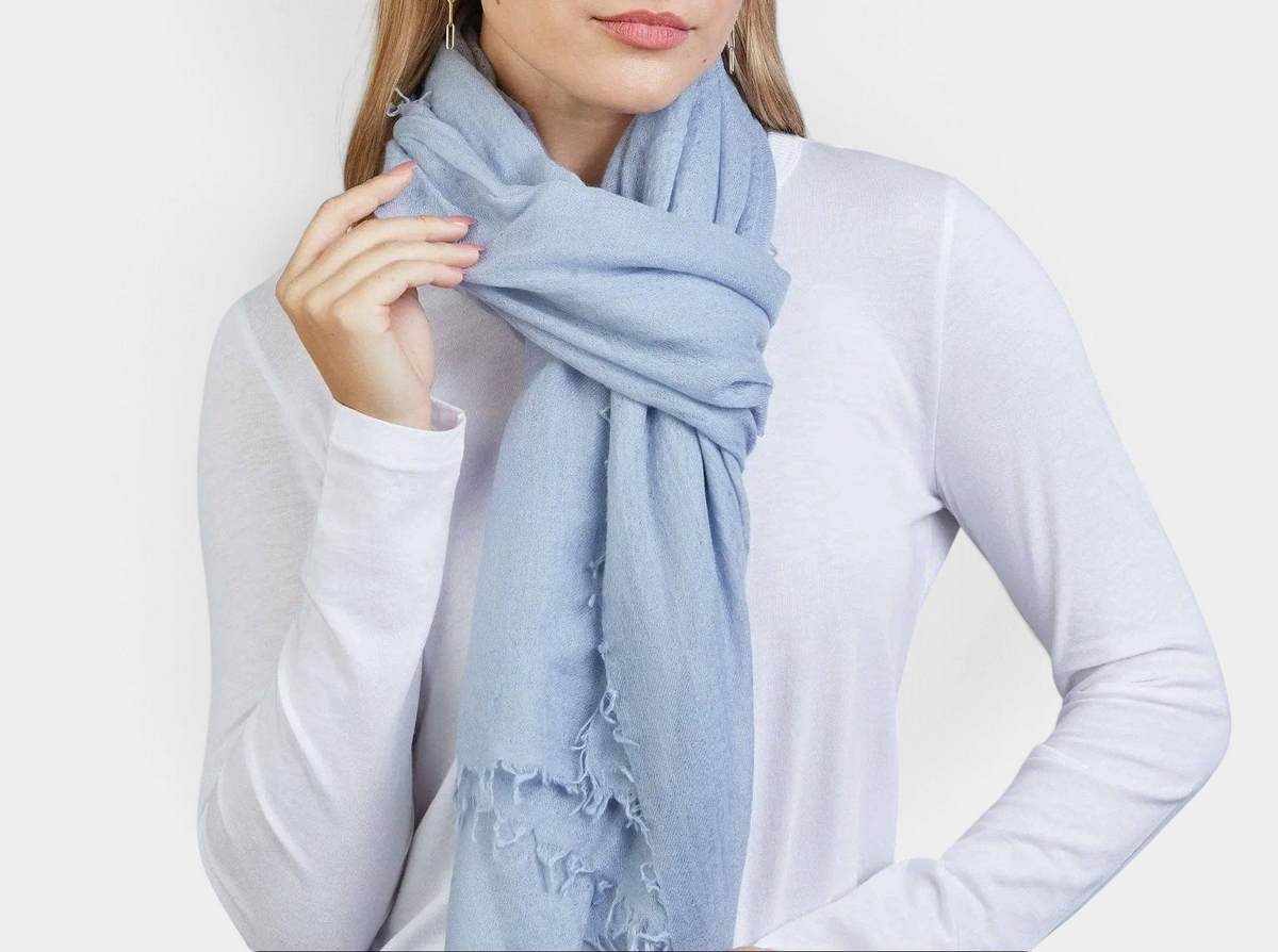 The Copper Shed arctic blue 100% Mongolian cashmere scarf with frayed edges worn by a woman in a white long-sleeve top