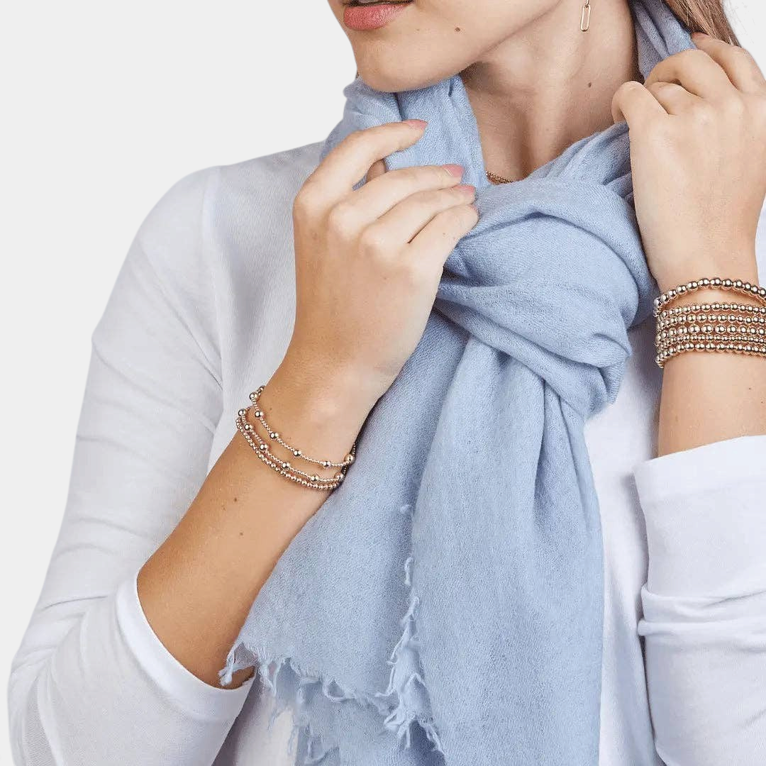 The Copper Shed arctic blue 100% Mongolian cashmere scarf draped around a model's neck with frayed edges.