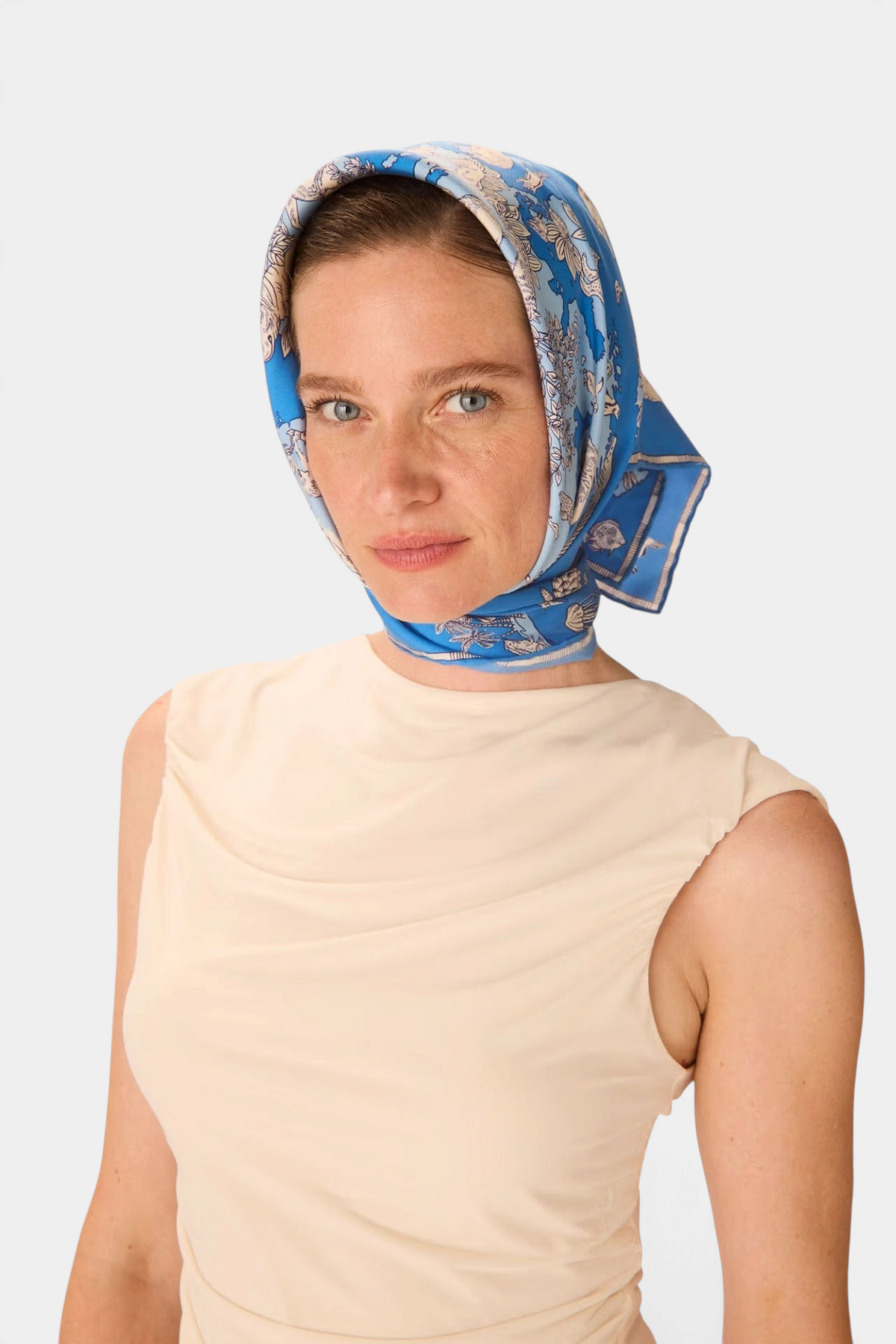 The Copper Shed Square 70 Atlas silk scarf in blue with floral patterns worn as a headscarf by a woman