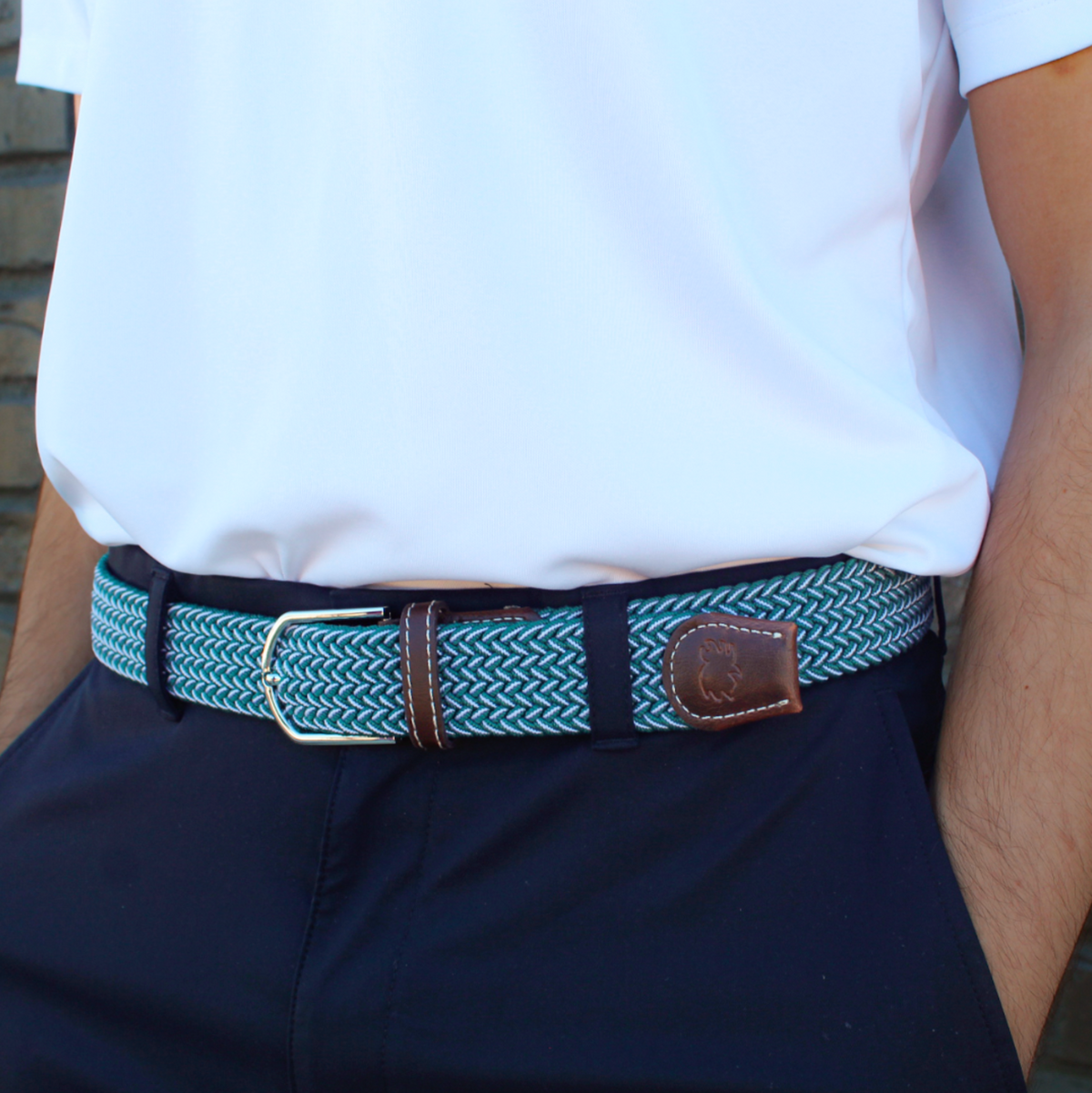 The Copper Shed Bandon green and white woven stretch belt with brown leather accents worn with navy trousers