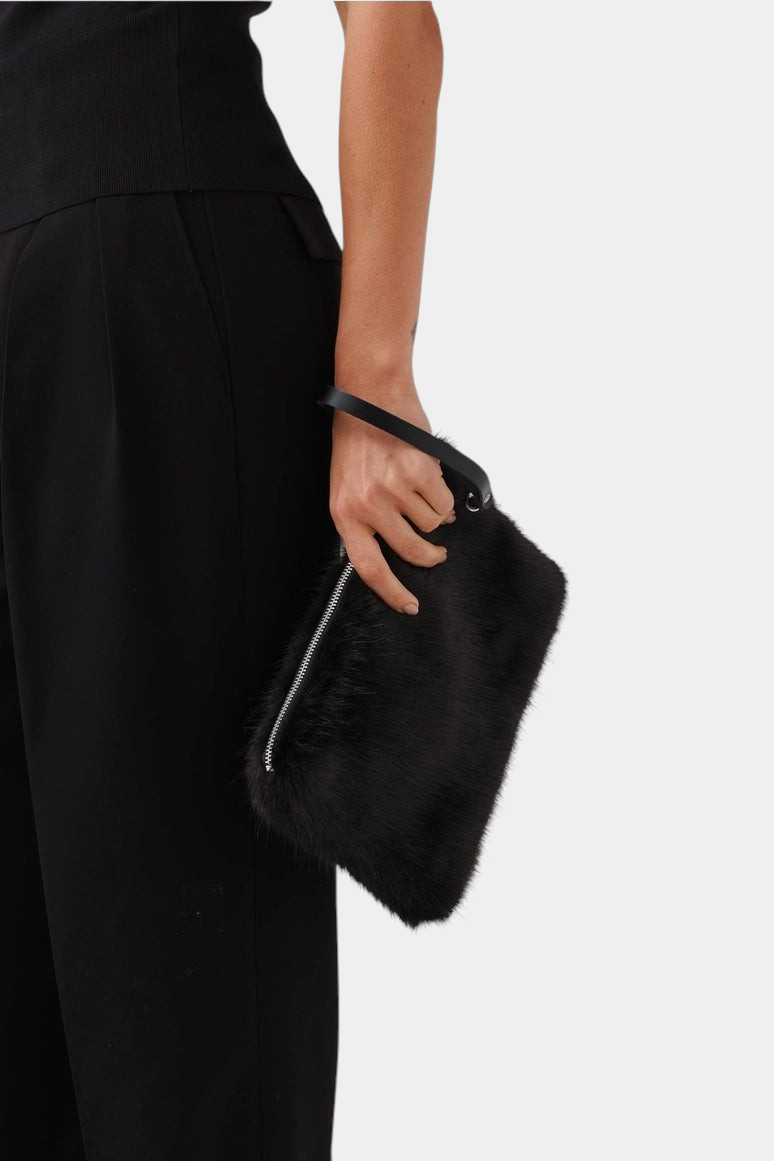 The Copper Shed black faux fur clutch bag with a detachable leather wrist strap held by a person in black clothing.