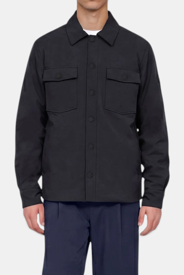 The Copper Shed men's black German jacket with patch pockets and snap-button closure worn over navy trousers.