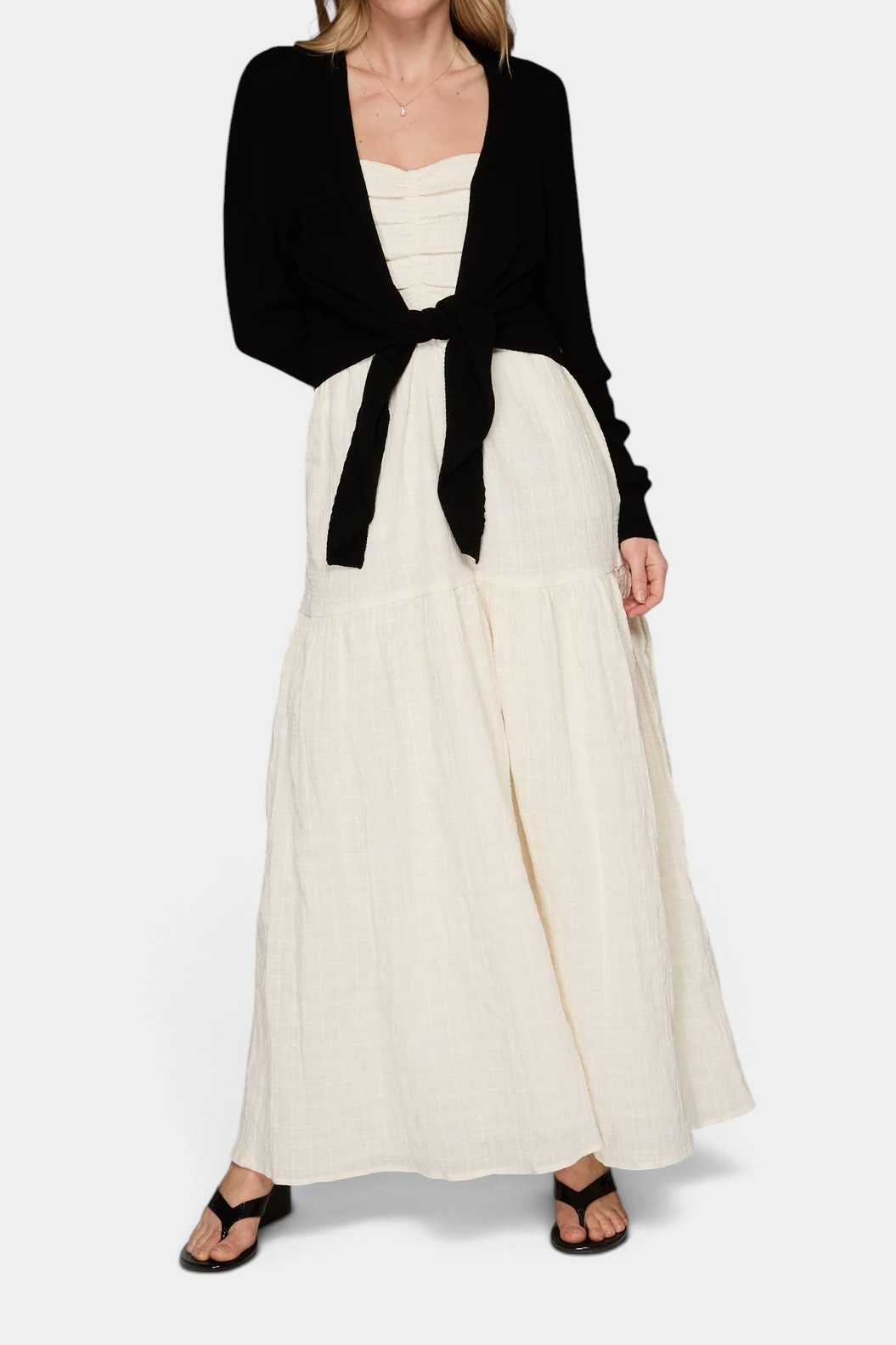 The Copper Shed black cashmere tie front rib cardigan worn over a cream maxi dress by a model