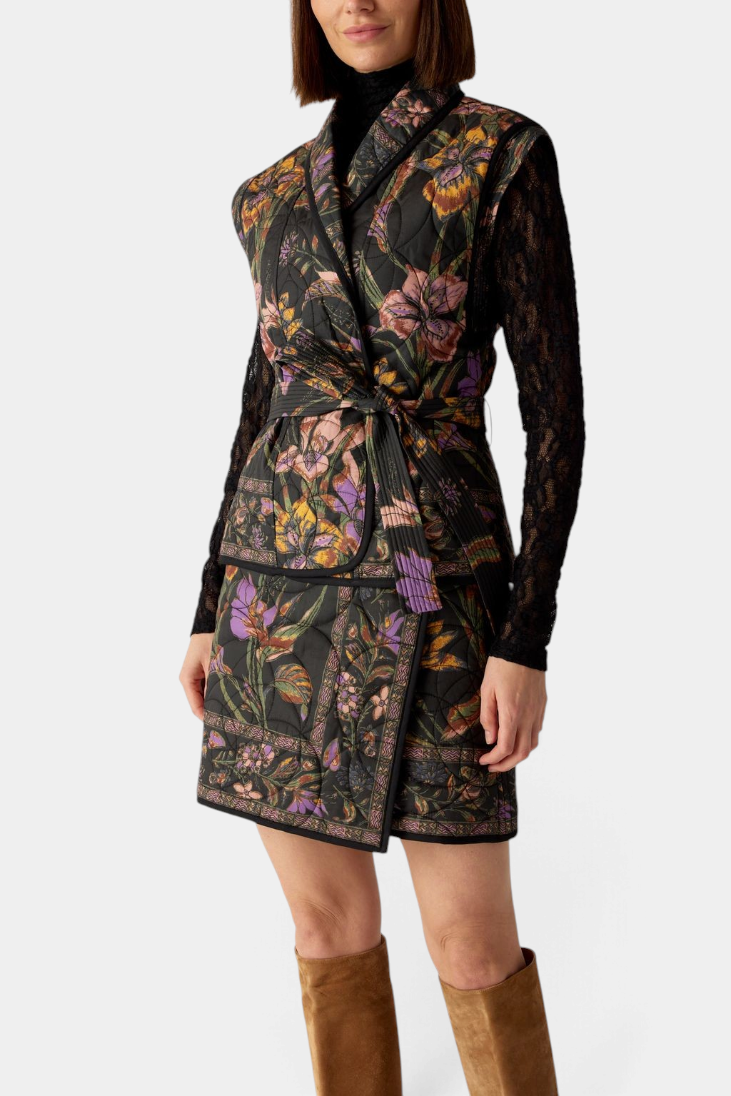 The Copper Shed Bowie vest in black floral quilted cotton with a shawl collar and wrap tie belt worn over a skirt.