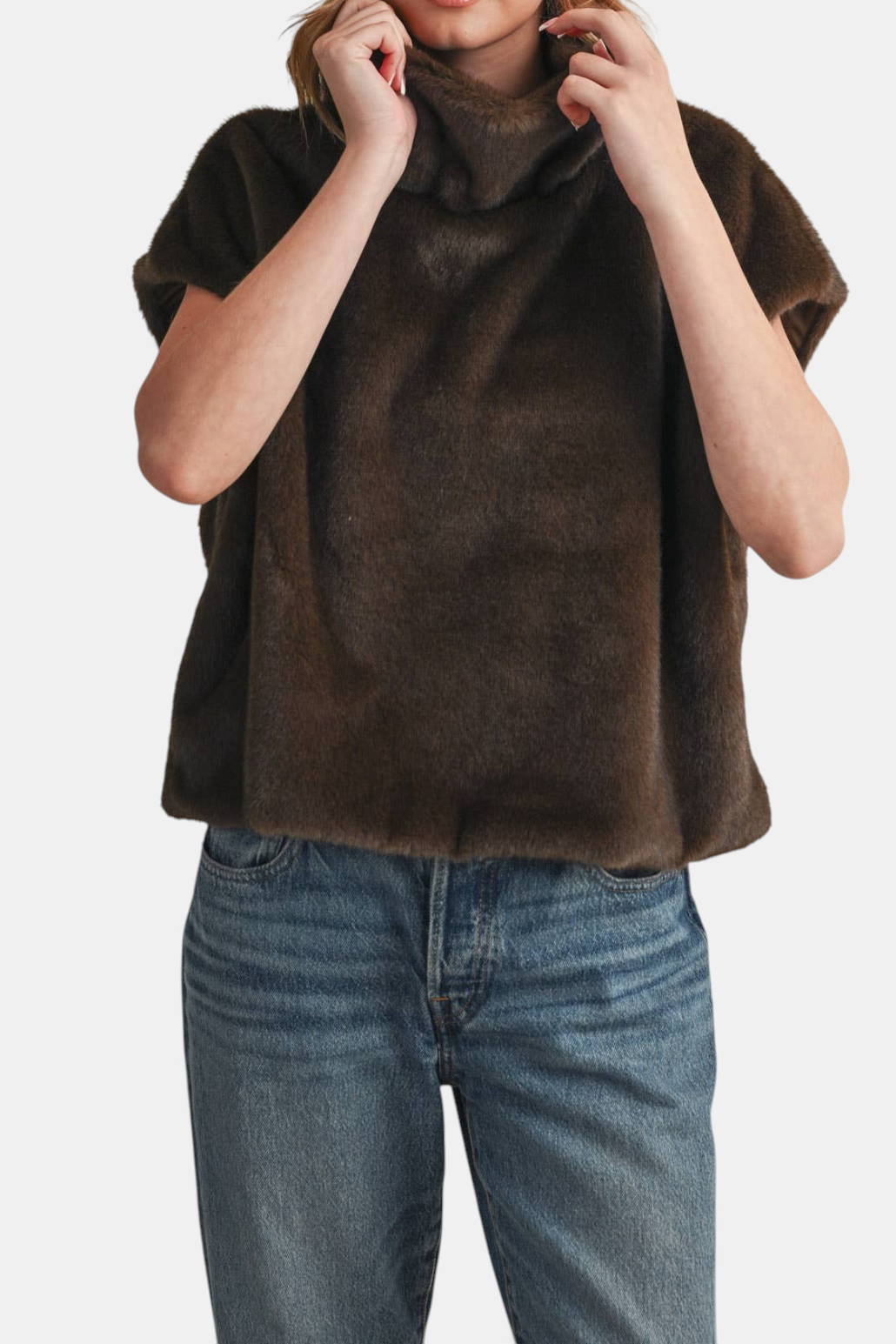 The Copper Shed brown faux fur cap sleeve turtleneck top with a relaxed fit and high-low hem worn with blue jeans.