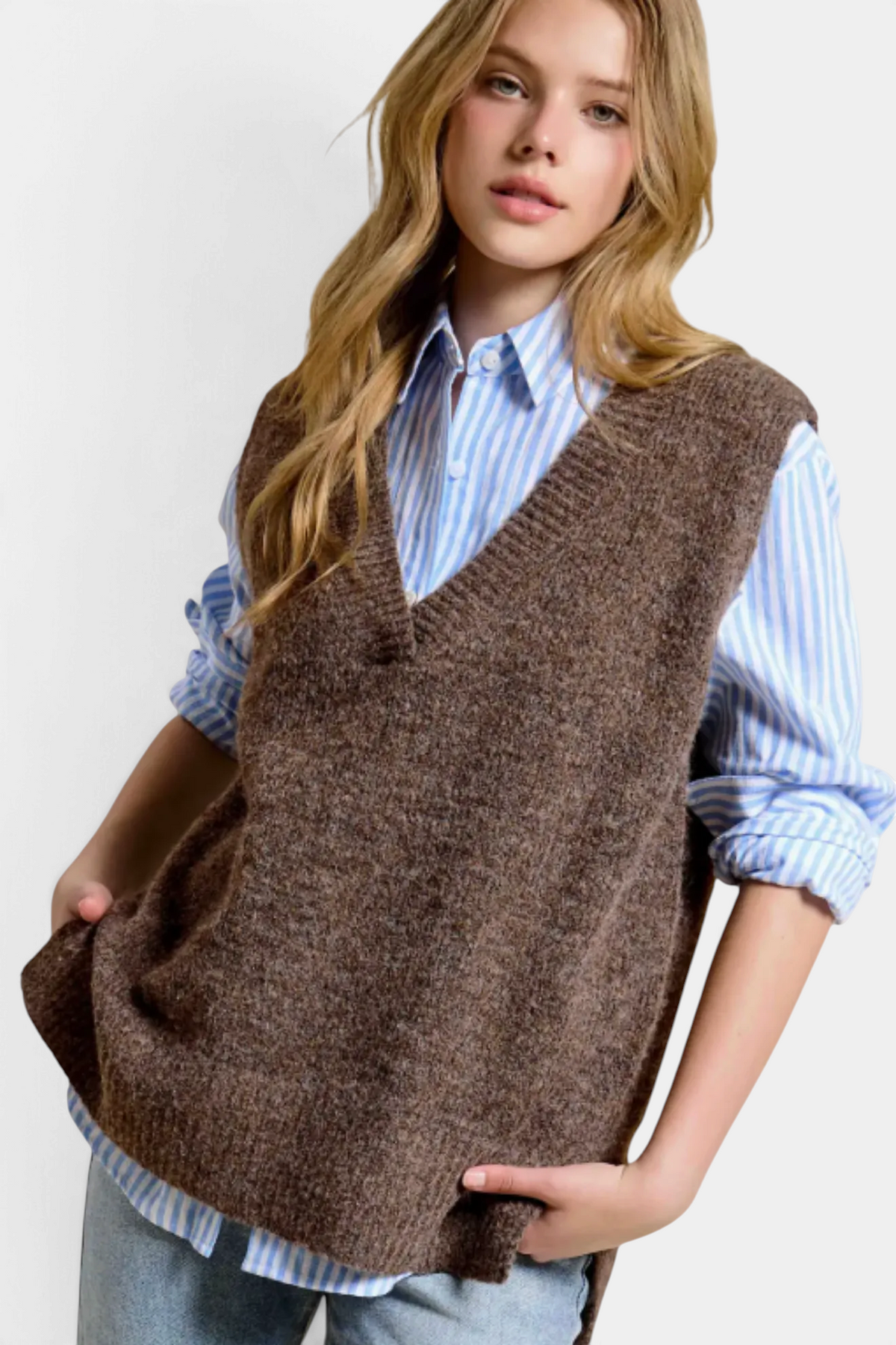 The Copper Shed brown oversized knit sweater vest with a v-neckline and side slits layered over a blue striped shirt.