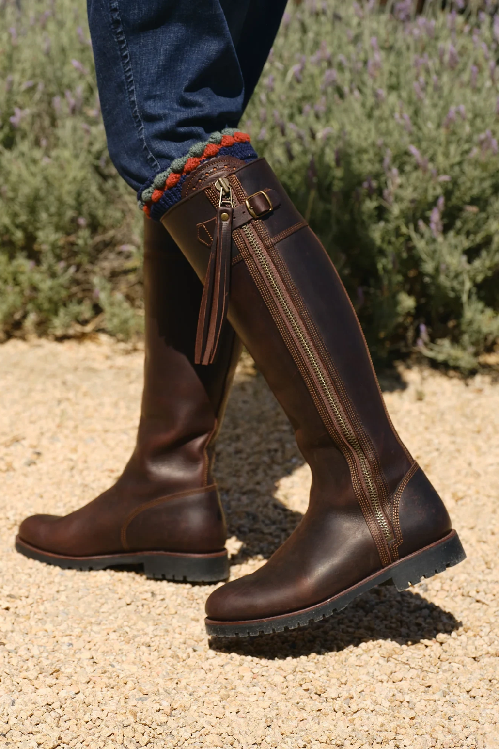 The Copper Shed brown leather knee-high tassel boots with side zip and Goodyear welted rubber sole worn with jeans.