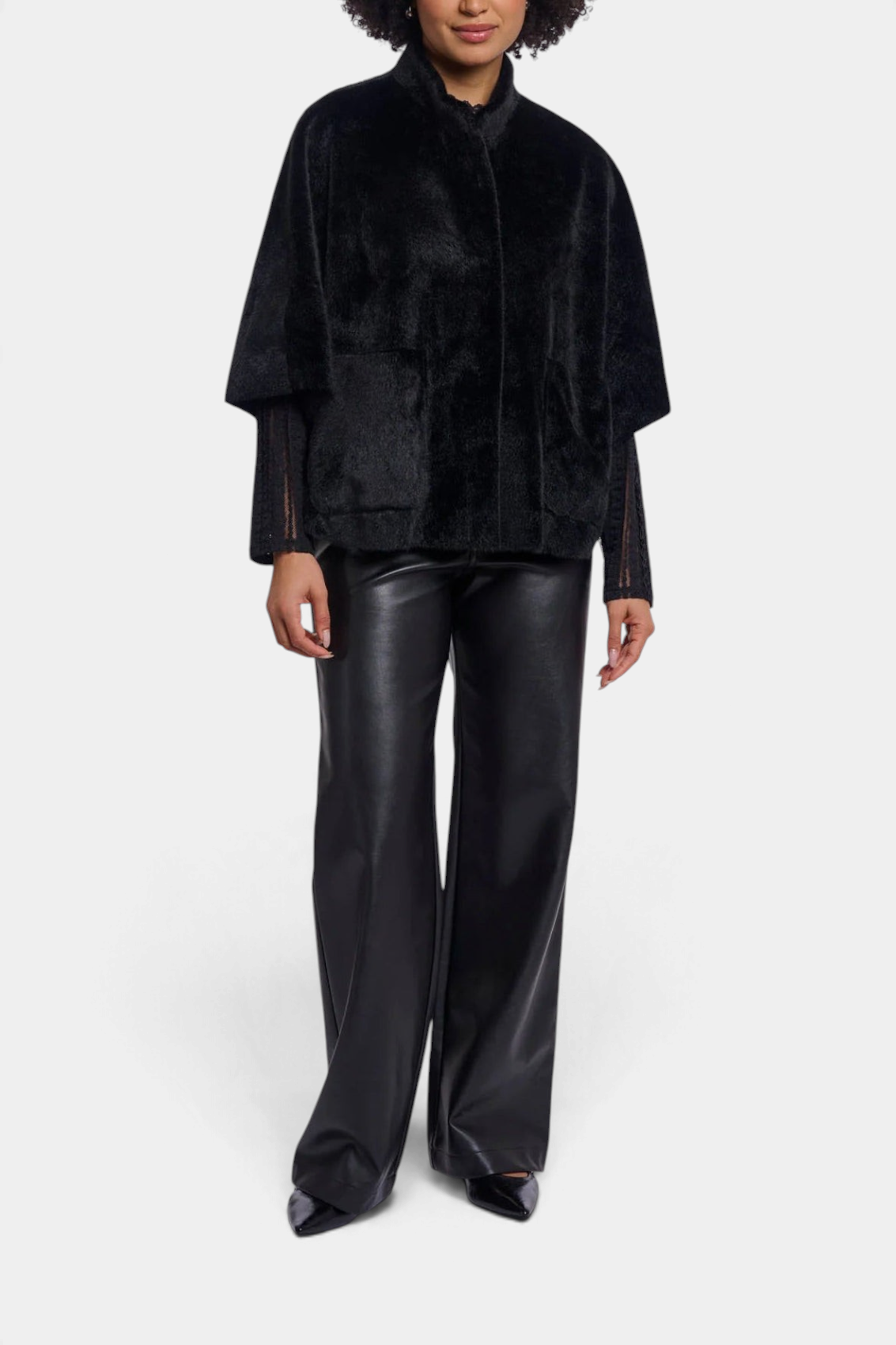The Copper Shed Dewi black faux fur cape with front pockets and button closure worn over black trousers