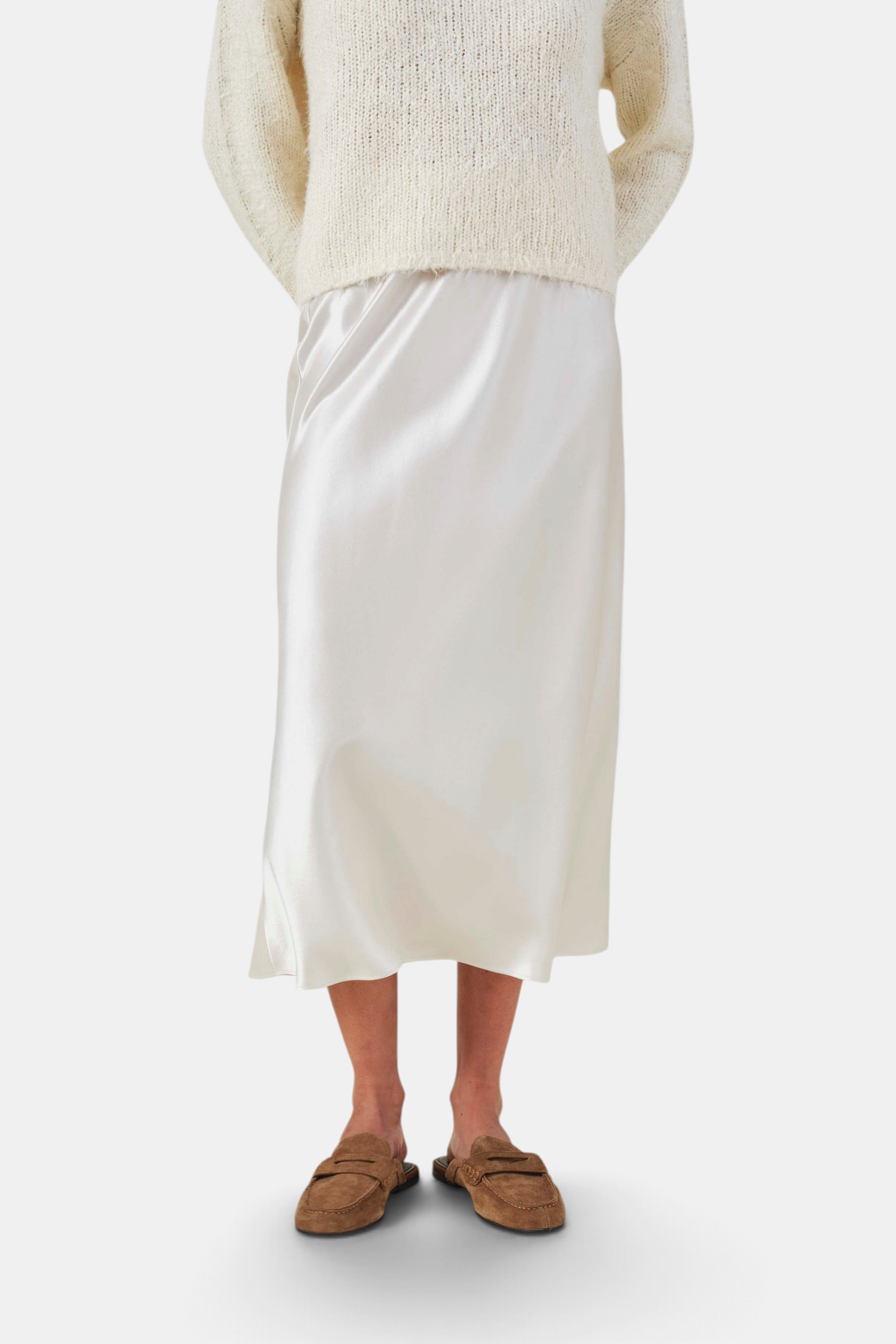 The Copper Shed Ella skirt in cream satin with a bias-cut silhouette and high-rise waist, styled with a knit sweater.