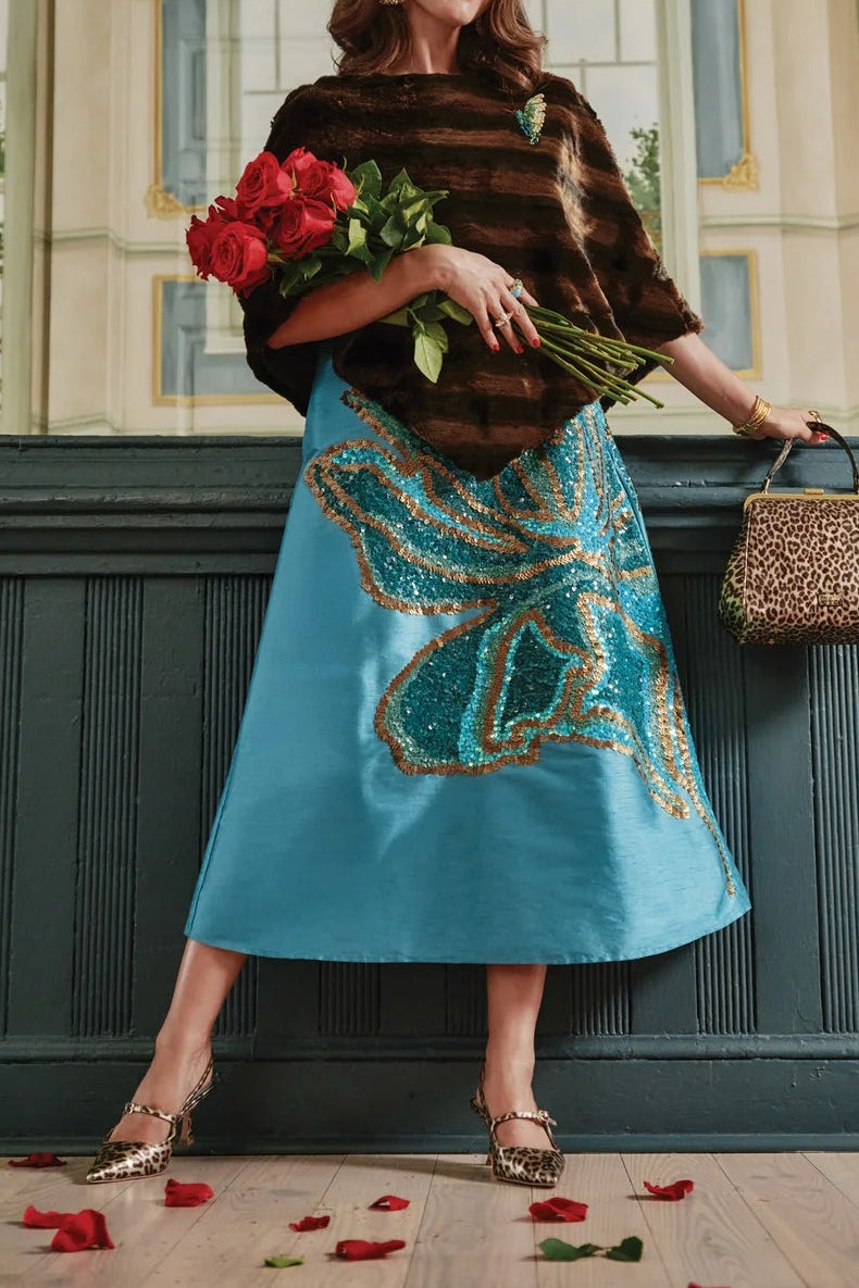 The Copper Shed Envoy brown faux fur poncho worn over a blue skirt with large sequin butterfly detail
