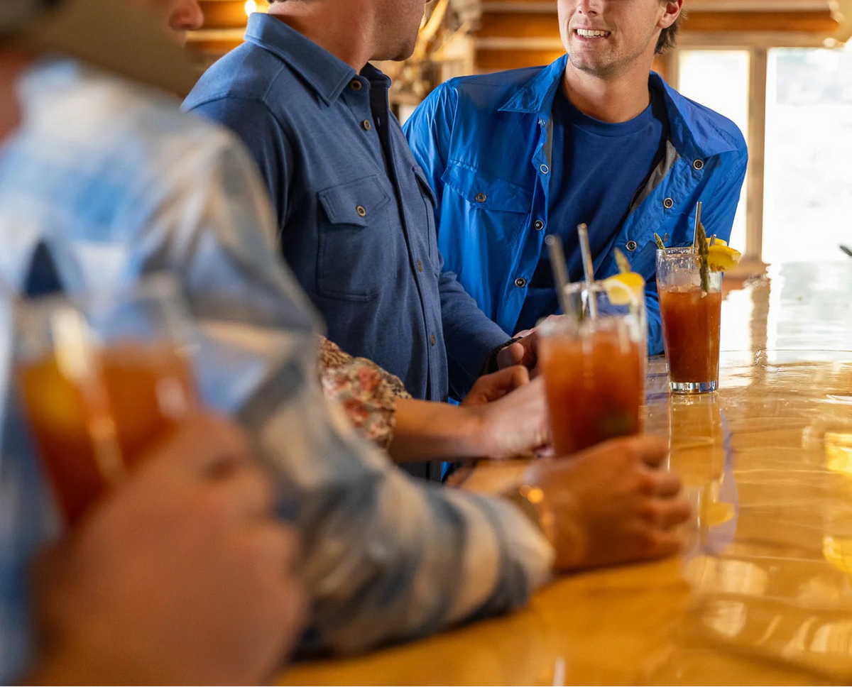 The Copper Shed Frigate Windshirt in bright blue worn by a man at a bar with friends.