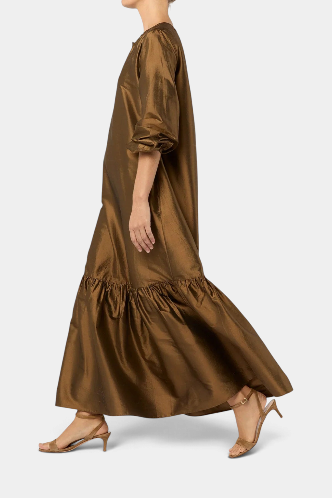The Copper Shed gold silk shantung maxi dress with tiered skirt and elastic cuffs worn by a model in profile view