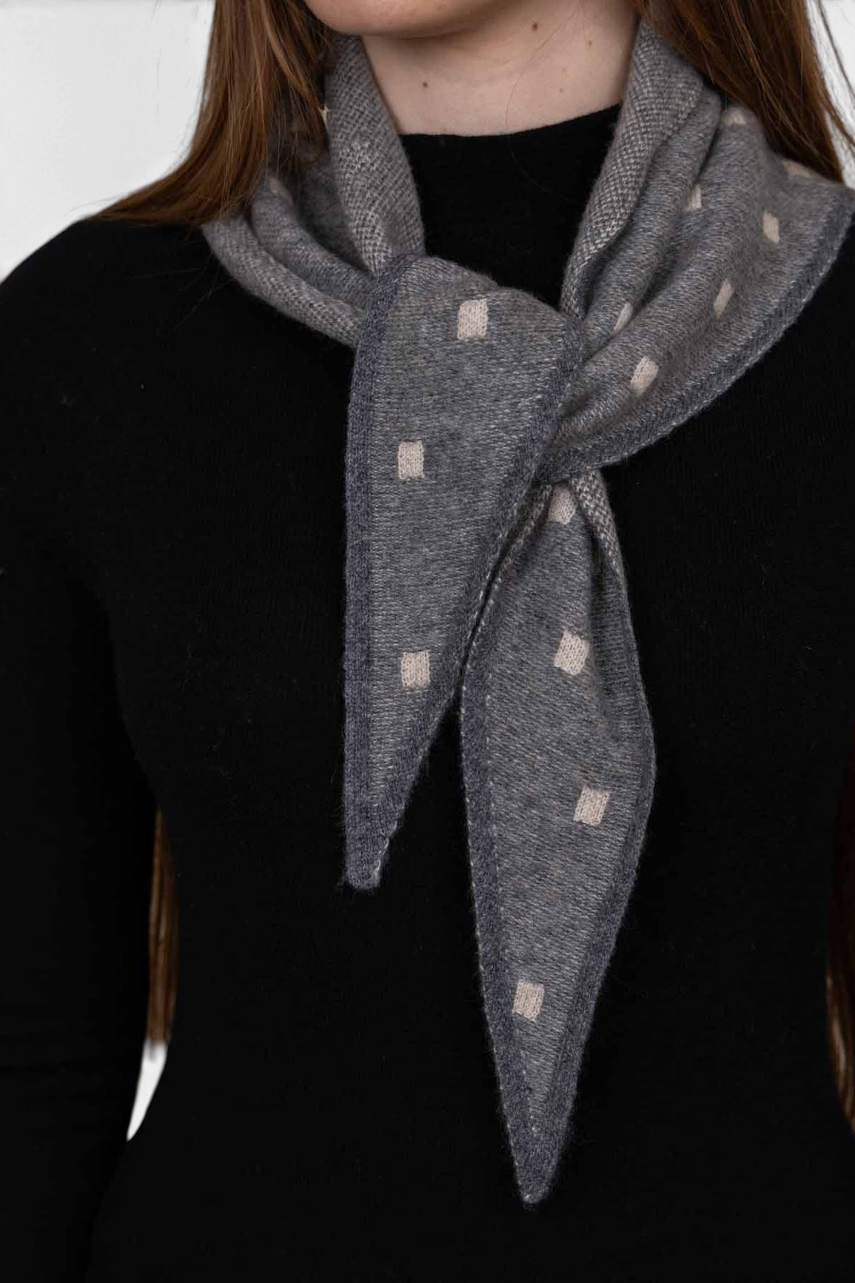 The Copper Shed Mia triangle cashmere neckerchief in grey with a subtle cream square pattern worn around the neck.