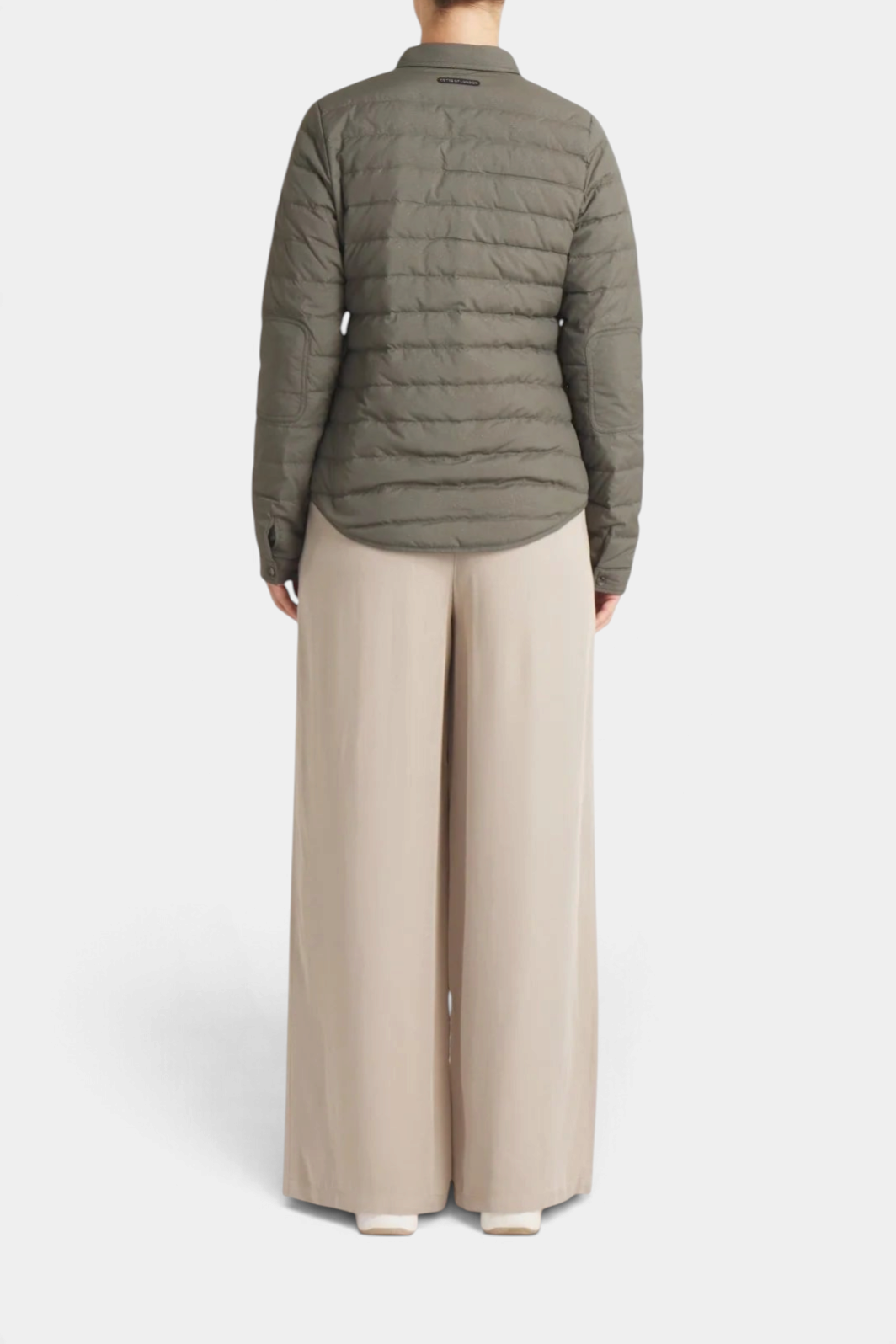 Back view of The Copper Shed Harrow matte olive green down shirt worn with wide-leg beige trousers.