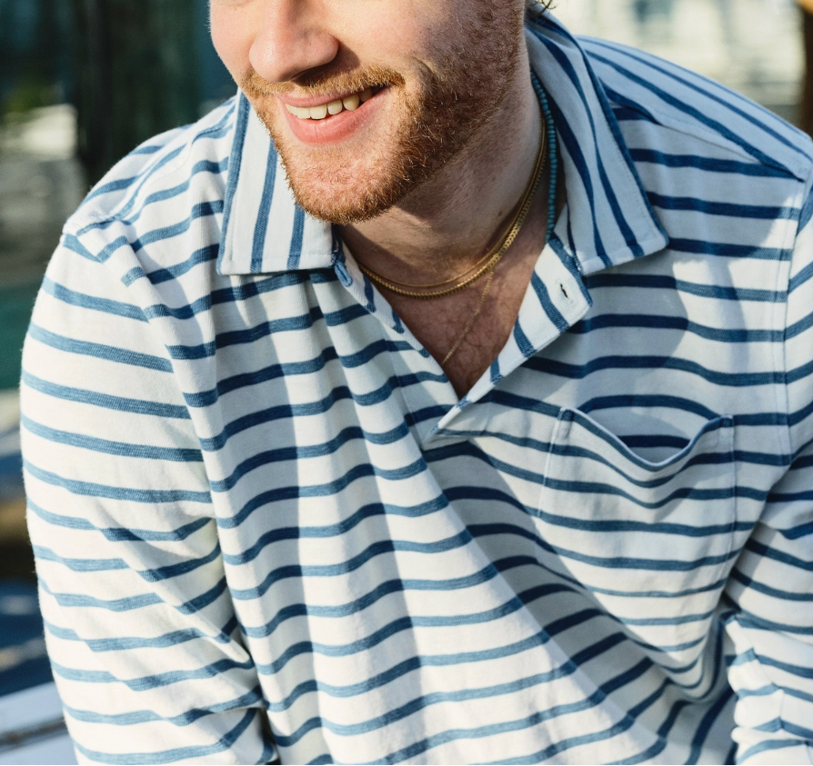 A man wearing a The Copper Shed long sleeve indigo striped cotton polo shirt with a one-button collar and chest pocket