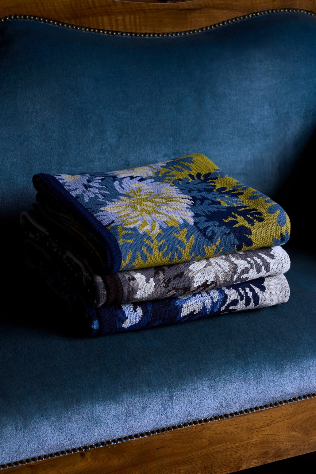 The Copper Shed Inoui Throw 130 cotton blankets featuring floral patterns in blue, yellow, and grey on a velvet chair.