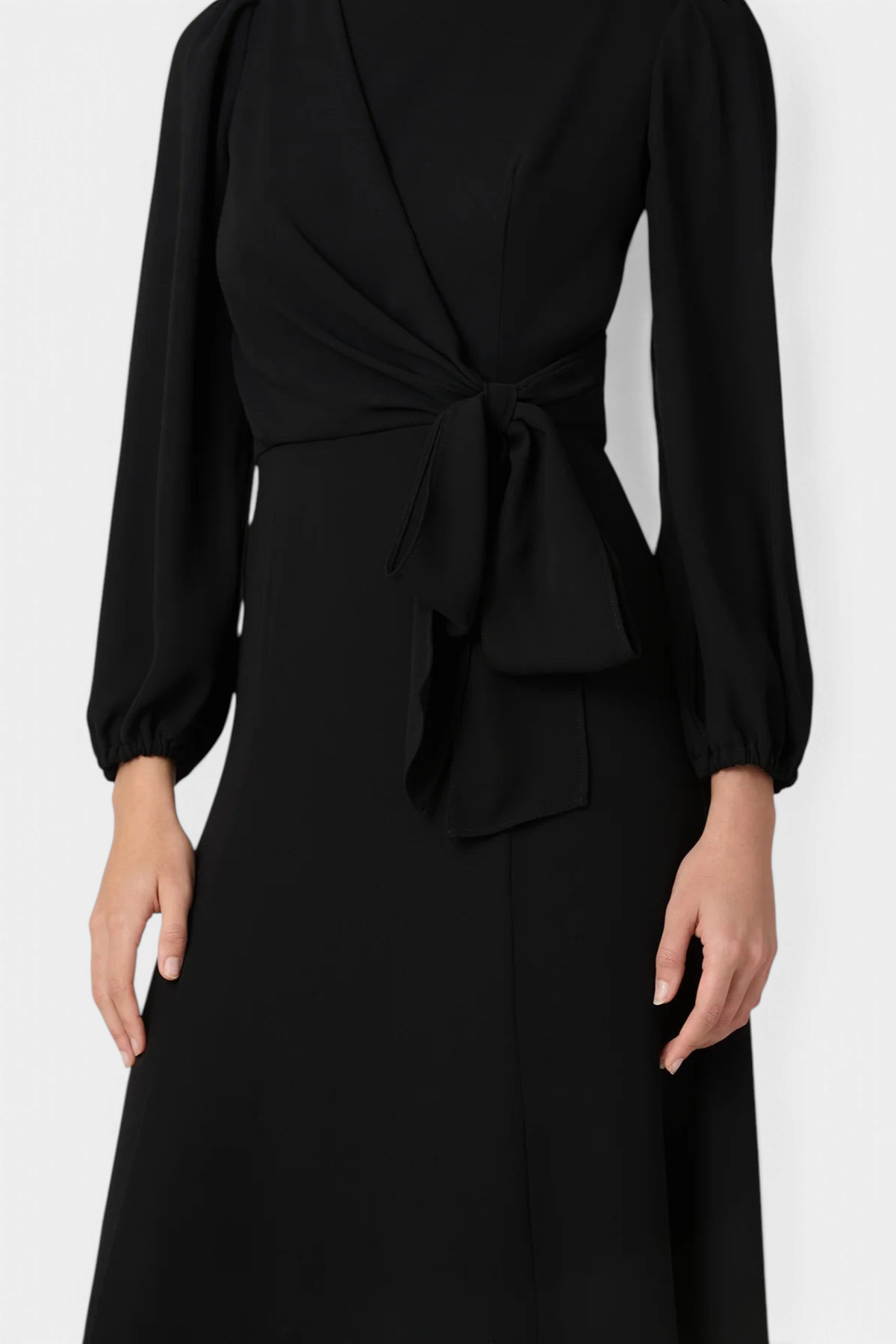 The Copper Shed Kathleen midi dress in black stretch crepe with long sleeves and an asymmetric bow waist detail.