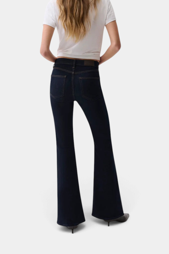 The Copper Shed Kinsley mid-rise ultra flare jeans in dark wash denim worn by a woman from the back view