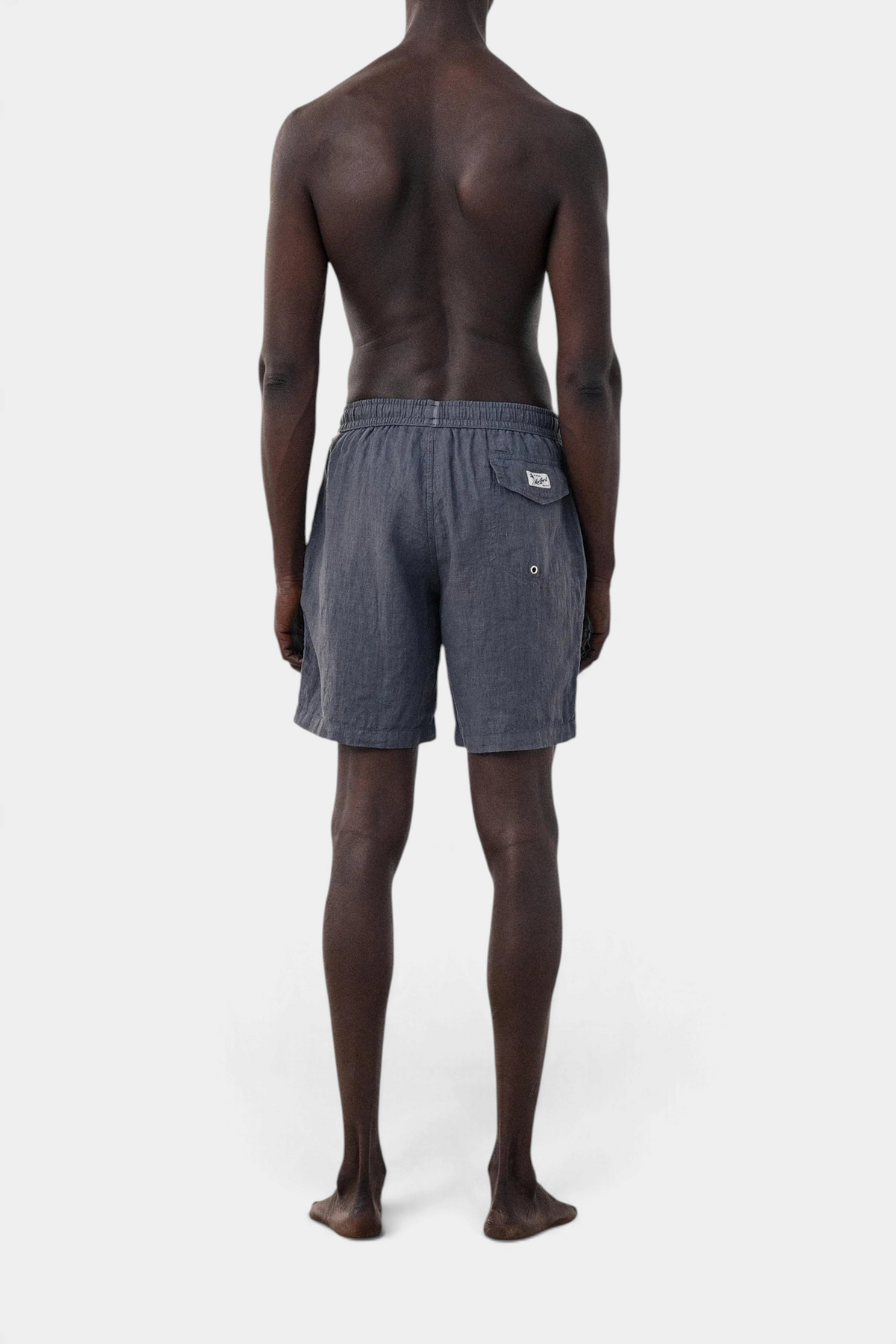 The Copper Shed long linen swim trunks in charcoal grey with an elastic waistband and back pocket, back view.