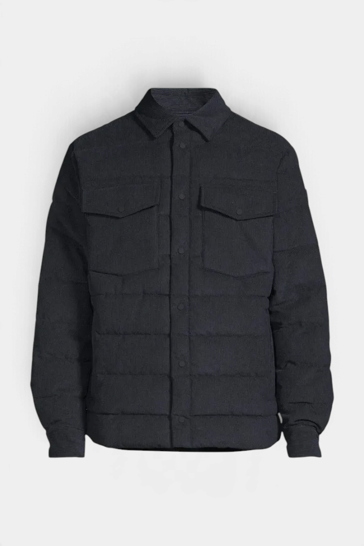 The Copper Shed Magnus jacket in black corduroy with a pointed collar, snap-button pockets, and a quilted puffer design.