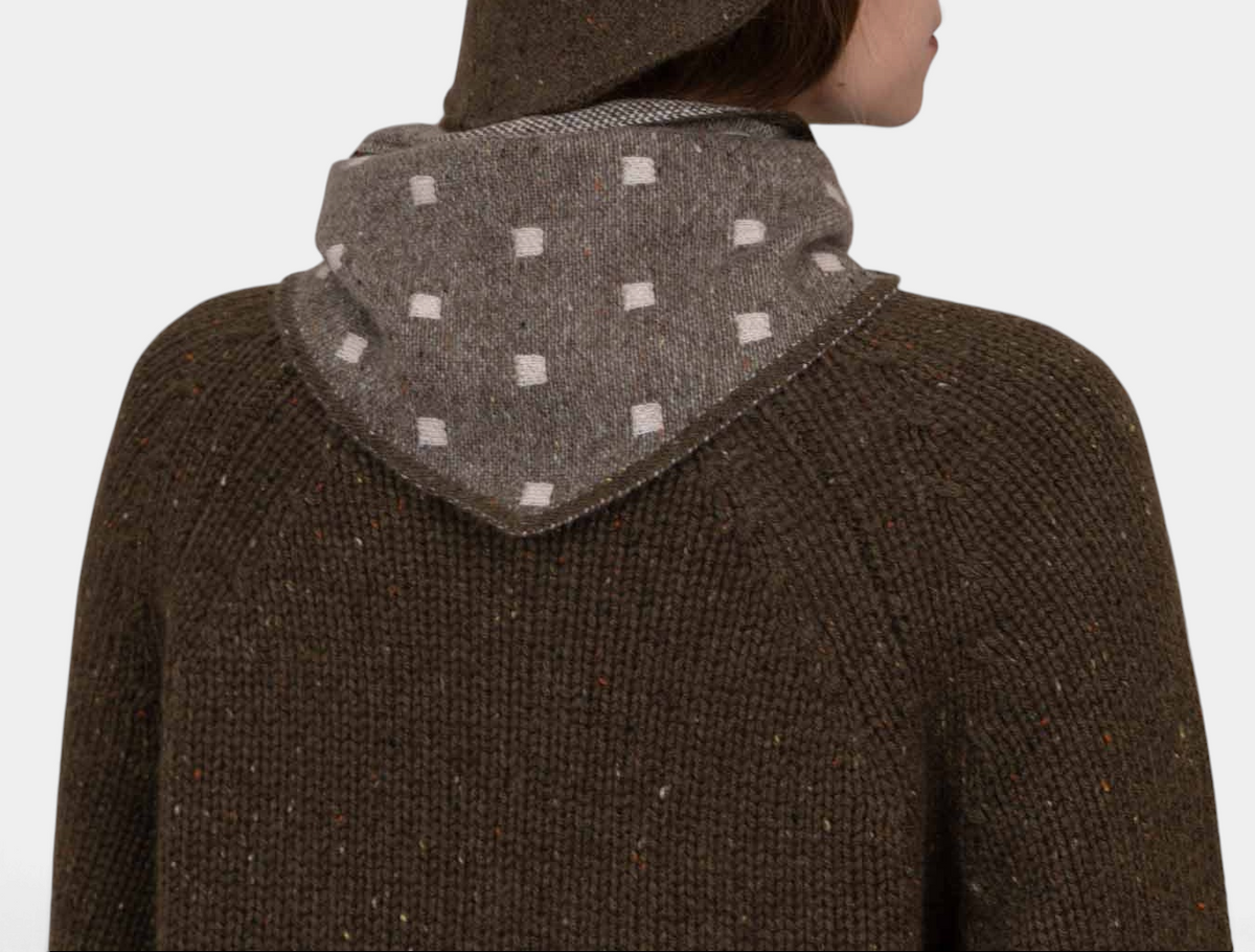 The Copper Shed Mia triangle cashmere neckerchief in brown with a white square pattern worn over a knit sweater