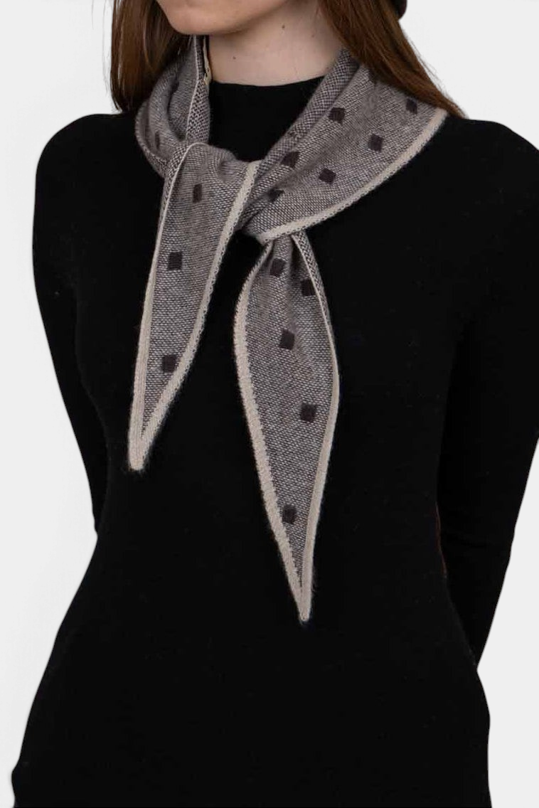 The Copper Shed Mia triangle cashmere neckerchief in grey with a subtle square pattern, worn tied around the neck.