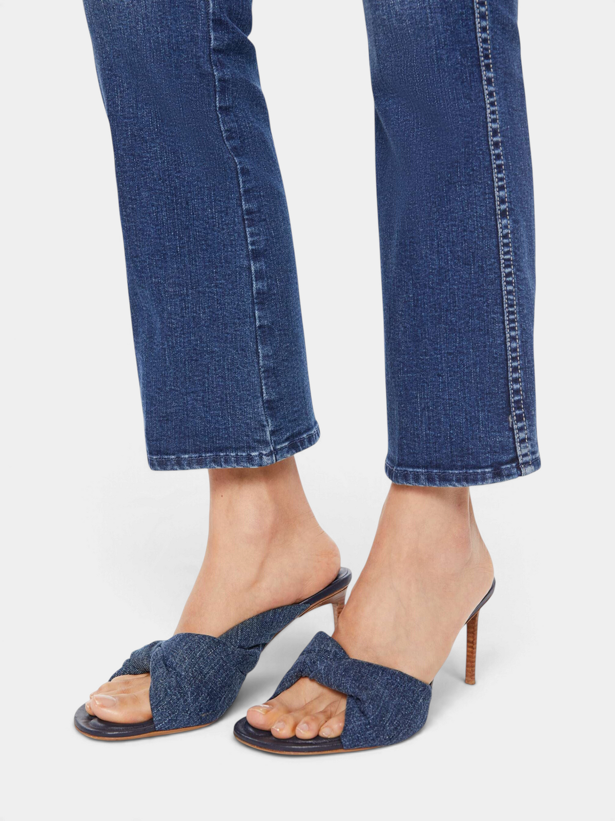 The Copper Shed mid-rise dark blue stretch denim jeans with a flared leg and clean hem worn with denim mule heels.