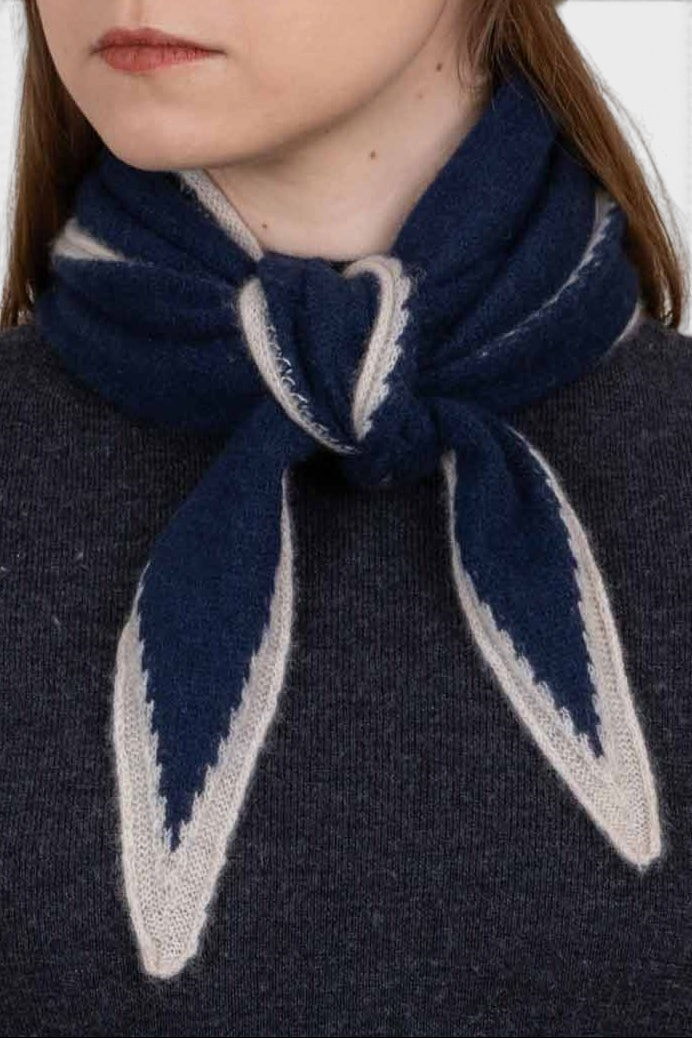The Copper Shed Austen spindle-shaped navy and beige organic cashmere scarf tied in a French knot around a model's neck.