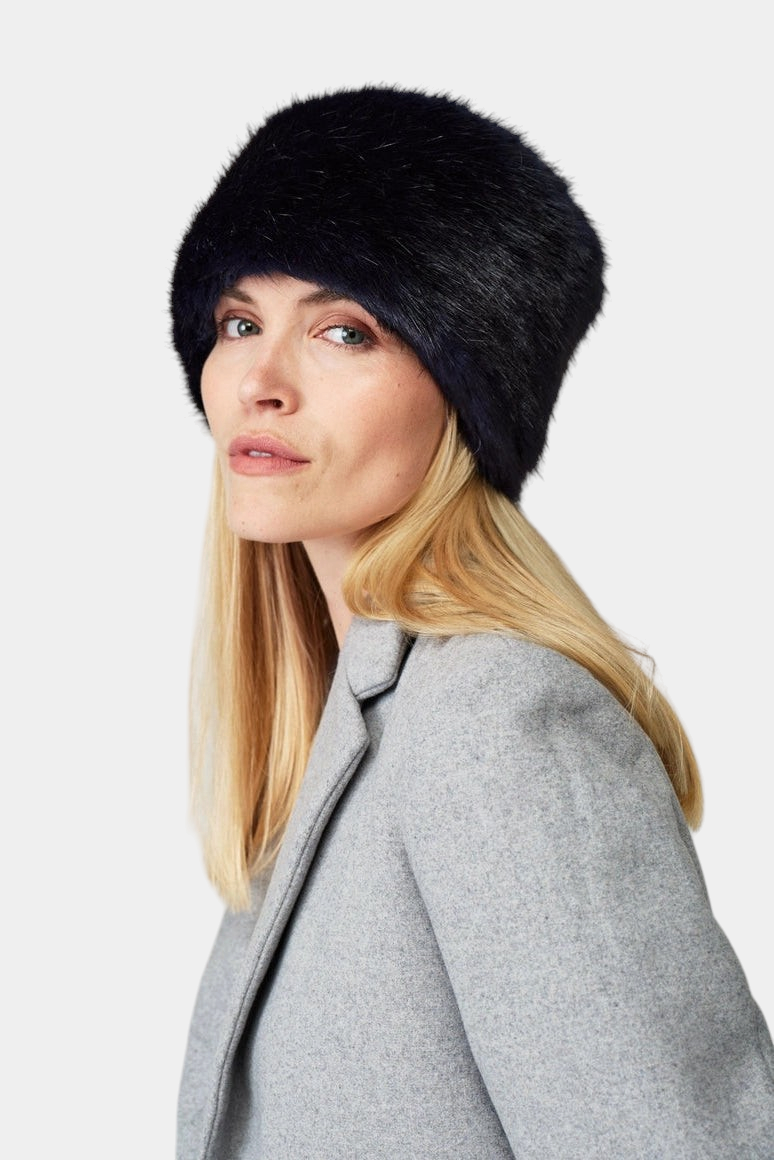 The Copper Shed navy blue faux fur pillbox hat worn by a woman with blonde hair in a grey coat