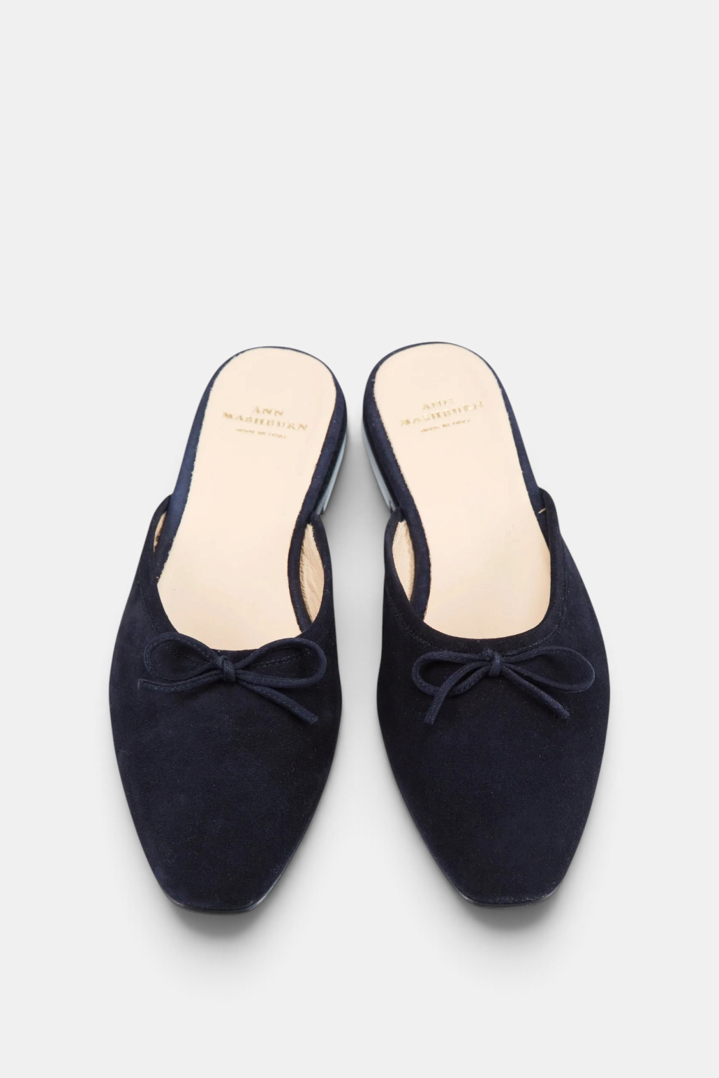 The Copper Shed navy kid suede Joy mules featuring a tapered almond toe, delicate bow detail, and low 10mm heel.