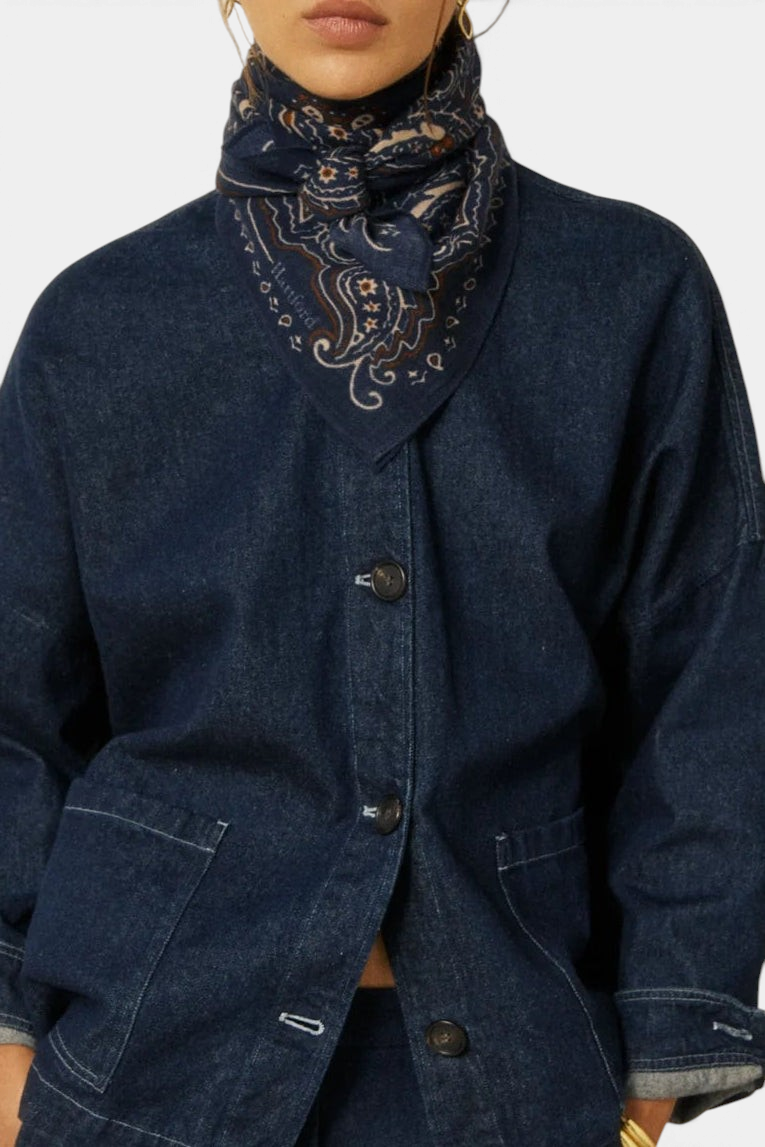 The Copper Shed paisley wool bandana in navy blue worn around the neck with a denim jacket.