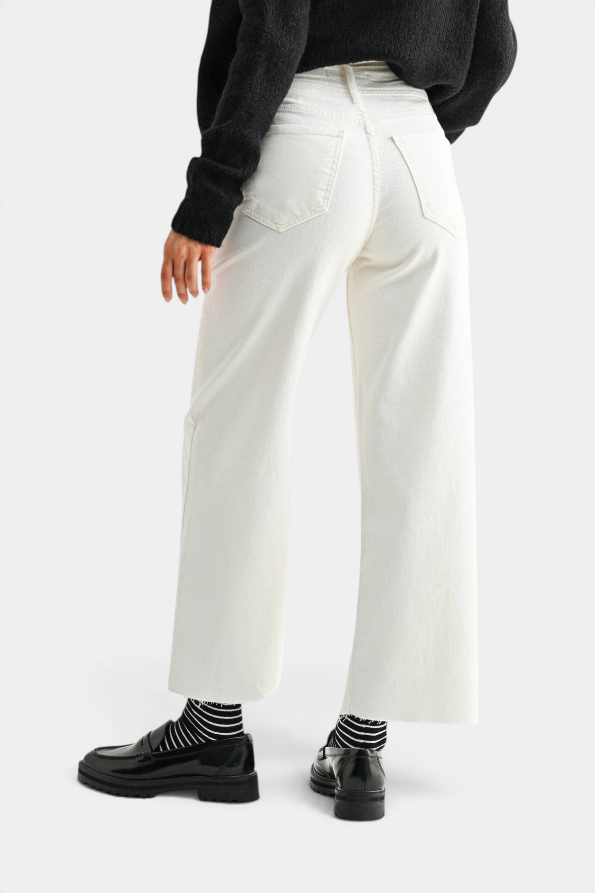 The Copper Shed high rise off-white wide leg jeans worn with a black sweater and black loafers, back view.