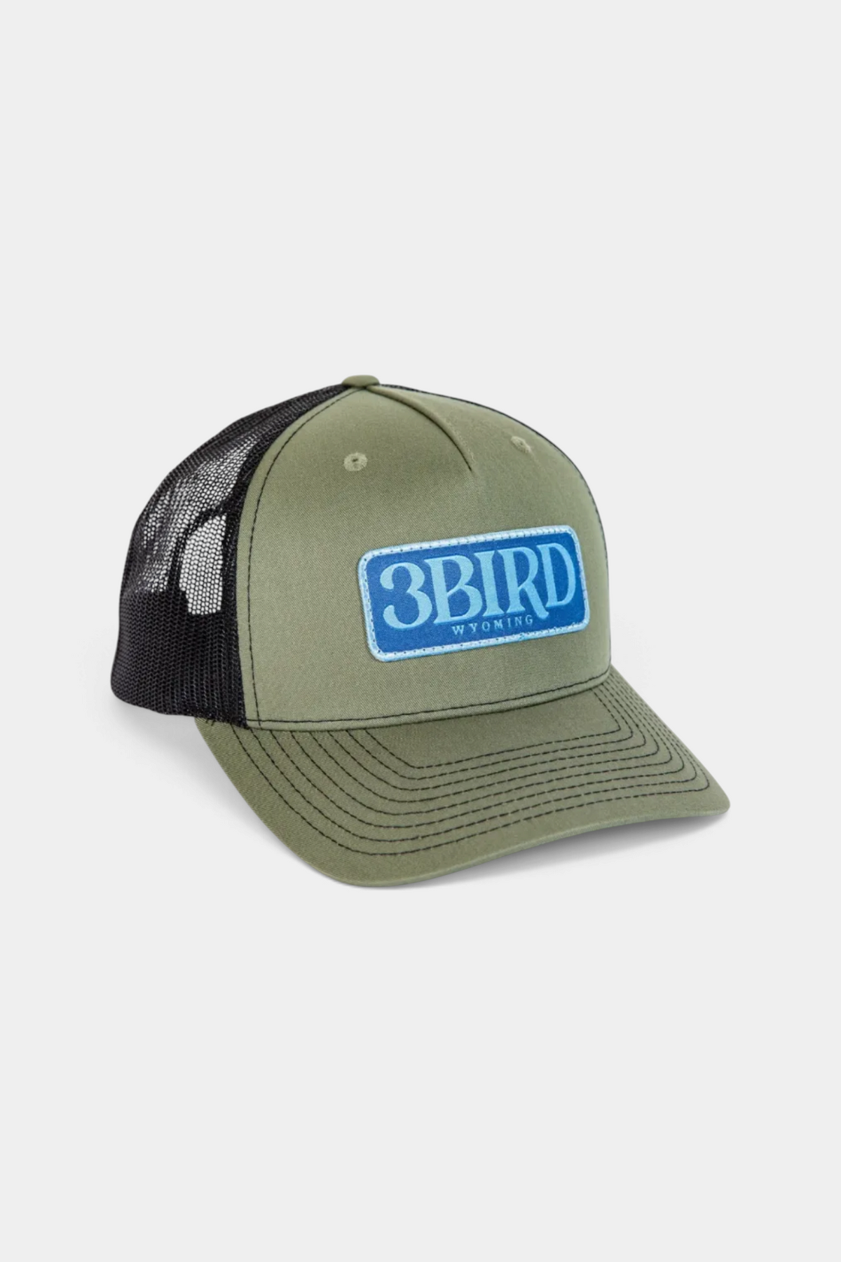 The Copper Shed 3B Trucker hat in olive green with a black mesh back and blue 3BIRD logo patch on the front.