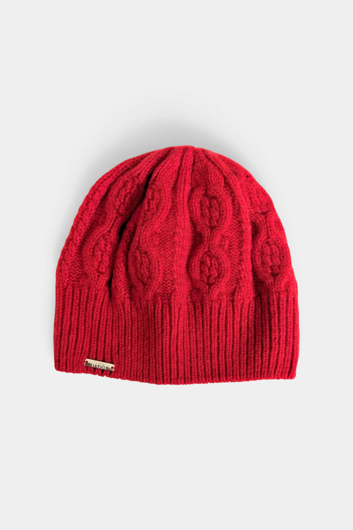 The Copper Shed red cable knit beanie made from a soft cashmere and merino wool blend with a small metal logo tag.